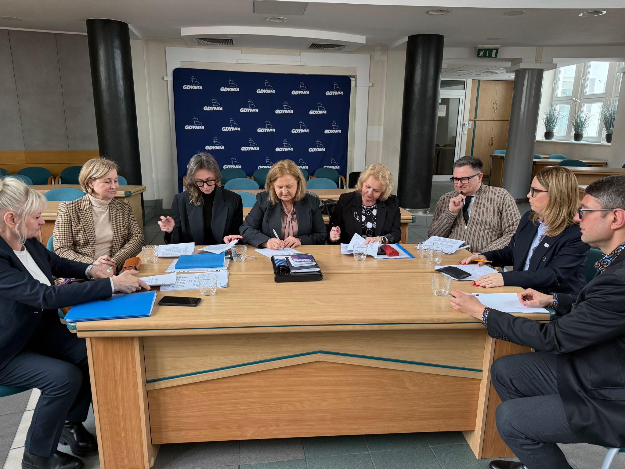 Sala obrad rady miasta w Urzędzie Miasta Gdyni, grupa os&oacute;b przy stole, na stole dokumentacja