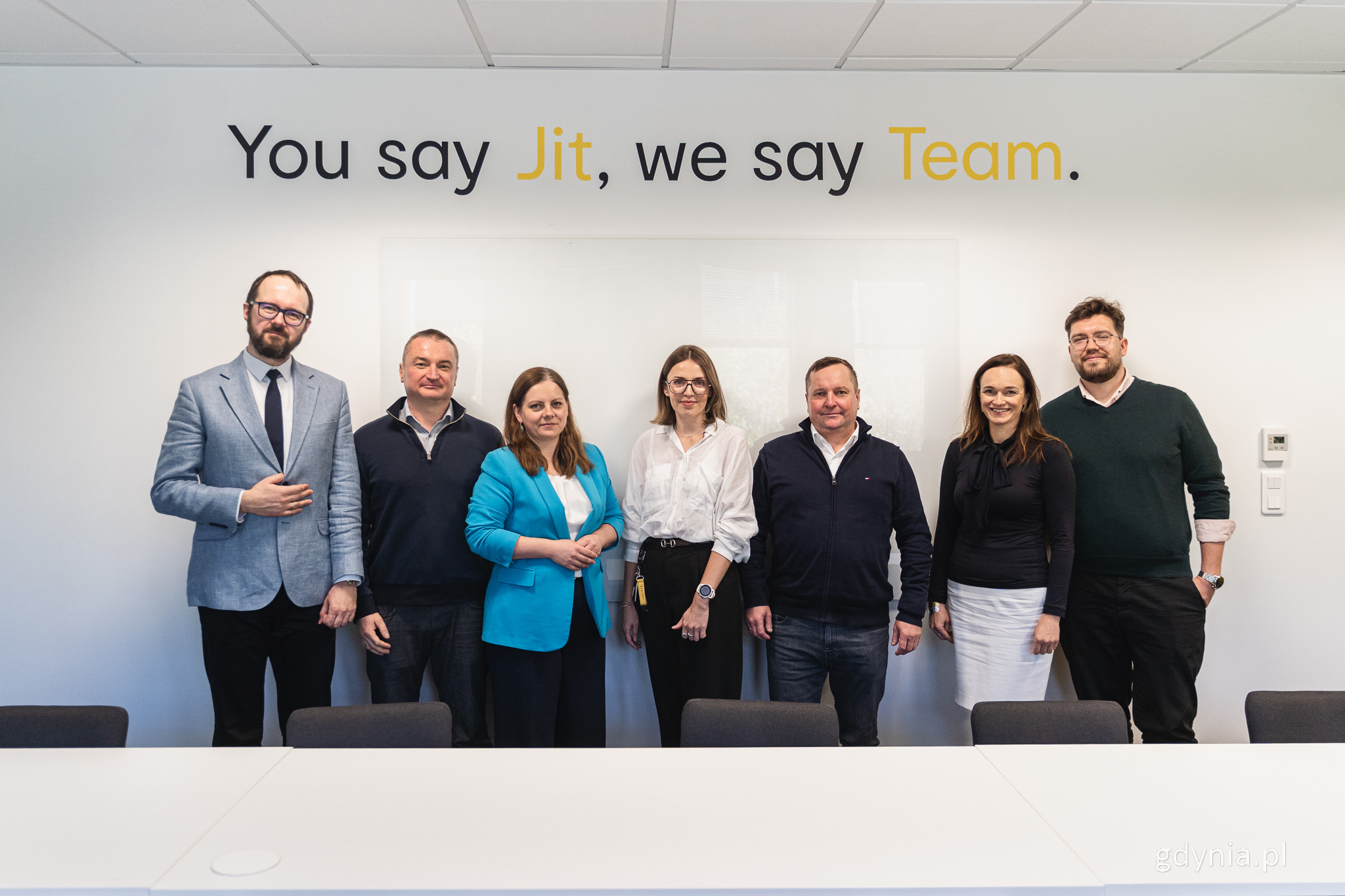 Grupa os&oacute;b pozuje do zdjęcia w sali konferencyjnej, nad nimi napis "You say Jit, we sam Team". Stoją, od lewej: Witold Bołt, Bartosz Cieśliński, Aleksandra Kosiorek, Magdalena Plewa, Mariusz Bessman, Izabela Disterheft, Rafał Proczek
