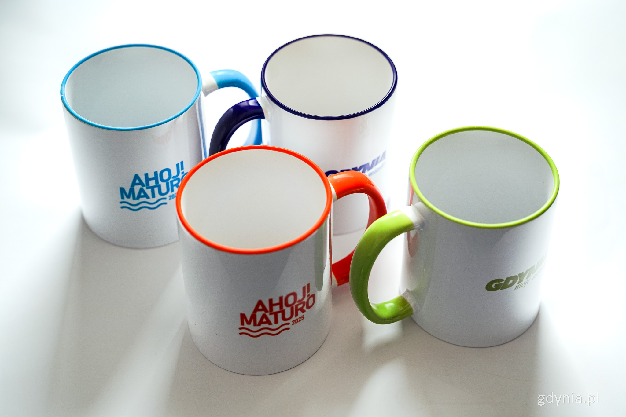 Białe tło, cztery kubki z kolorowymi obw&oacute;dkami: niebieską, ciemnoniebieską, zieloną i pomarańczową