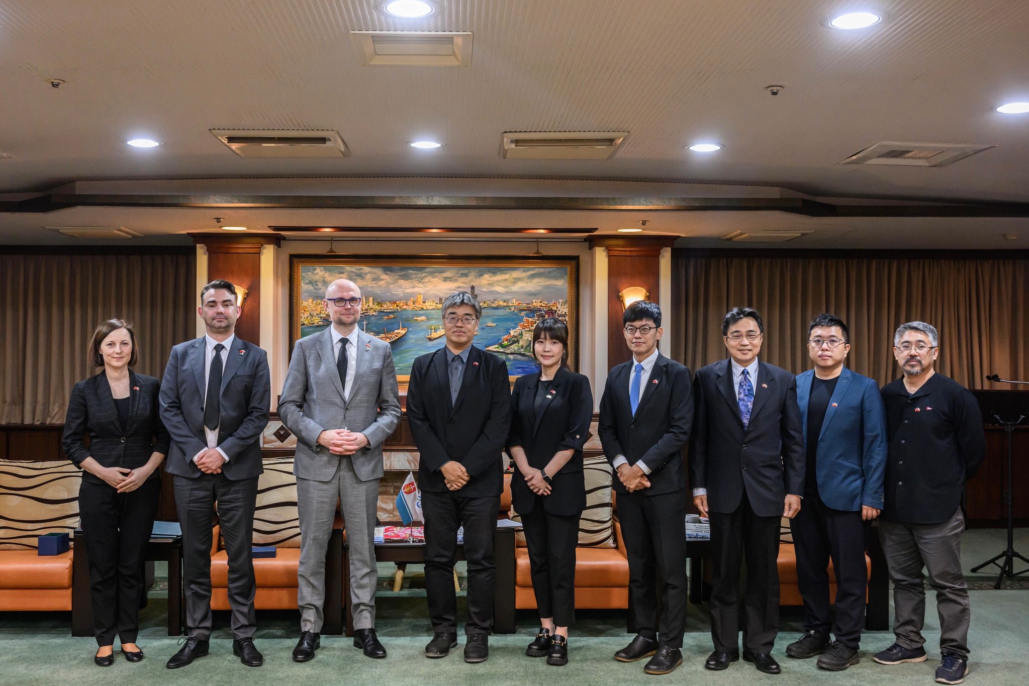Grupa os&oacute;b pozuje do zdjęcia w sali należącej do władz miasta Kaohsiung. Z lewej strony stoją Justyna Patyk, Piotr Wiśniewski i Bartłomiej Auten, dalej przedstawiciele miasta z Tajwanu