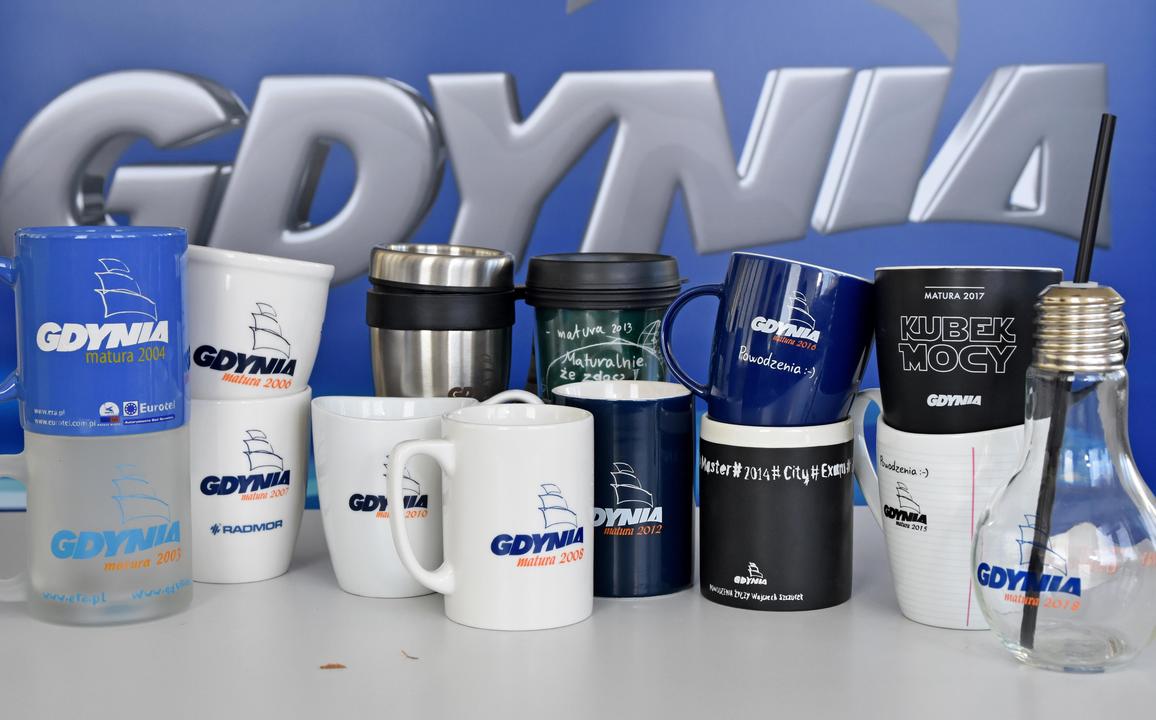 St&oacute;ł, rollup z napisem Gdynia, na stole kilkanaście r&oacute;żnych kubk&oacute;w dla maturzyst&oacute;w z Gdyni