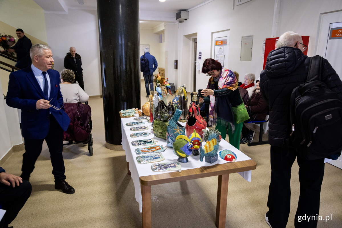 Na korytarzu przychodni stoi st&oacute;ł z ekspozycja ceramiki, wok&oacute;ł ludzie.