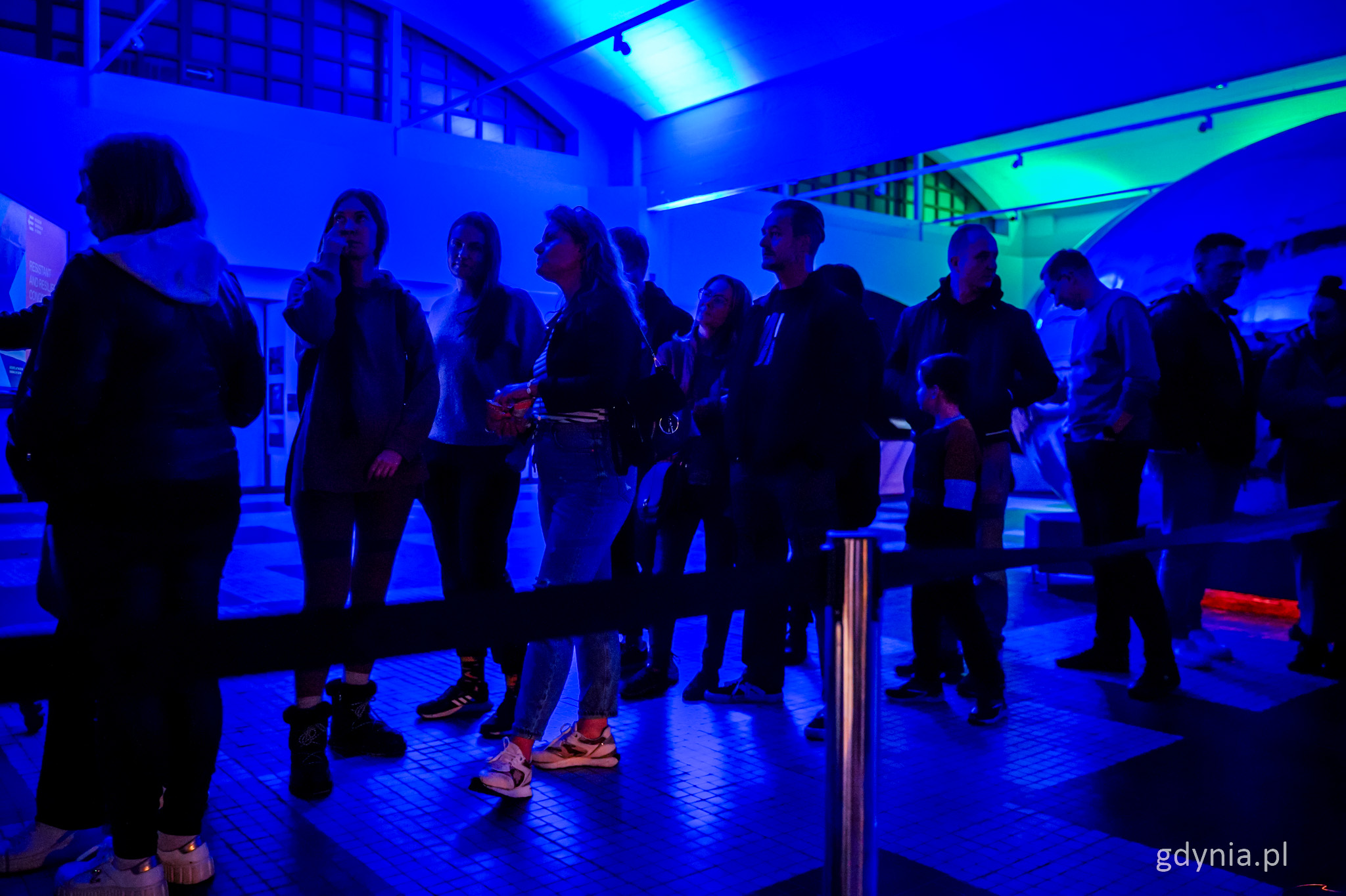 Wnętrze Muzeum Emigracji, ciemno, niebieskie światło, kolejka ludzi do wejścia