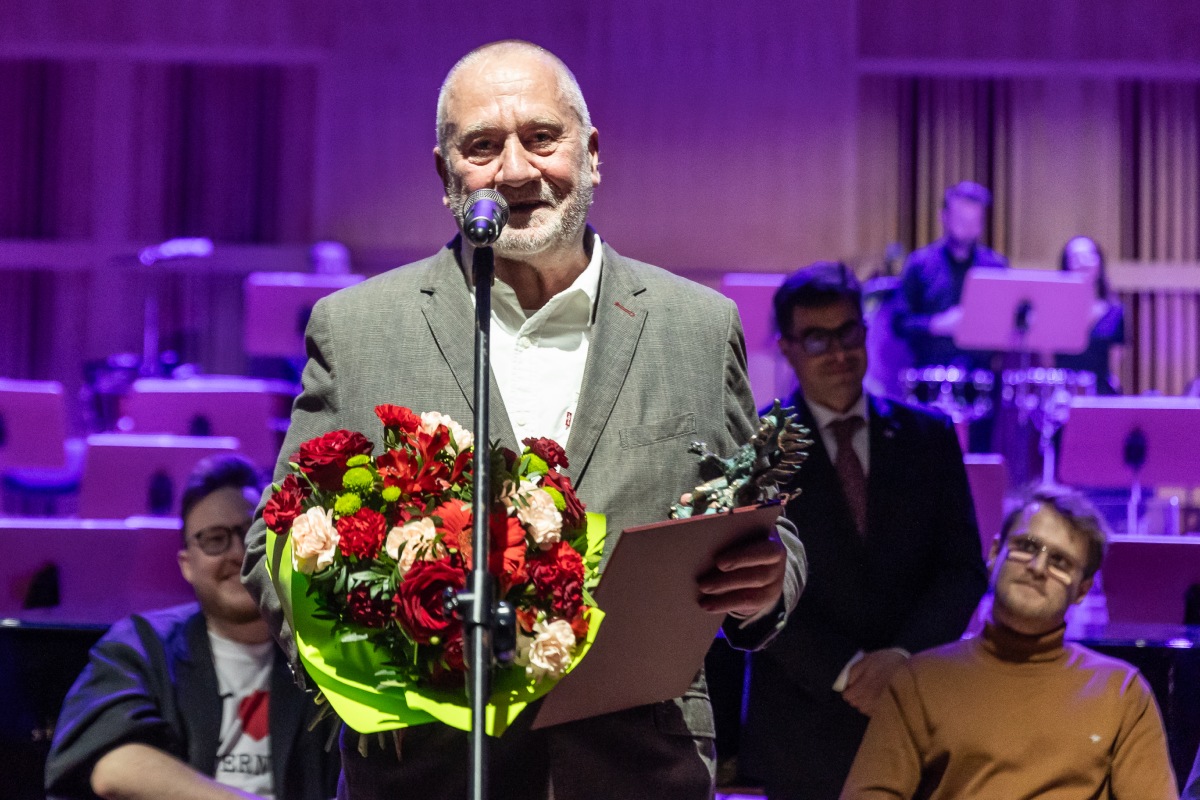 Andrzej Umiastowski podczas gali Pomorskiej Nagrody Artystycznej. Stoi przy mikrofonie, w rękach trzyma kwiaty oraz statuetkę (fot. Piotr Żagiell)
