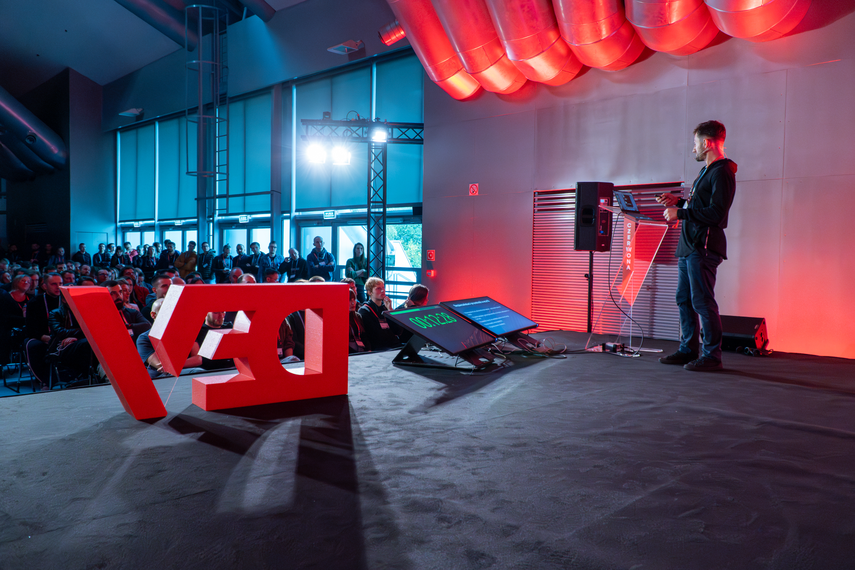 Mężczyzna stojący na scenie i przemawiający do grupy słuchaczy