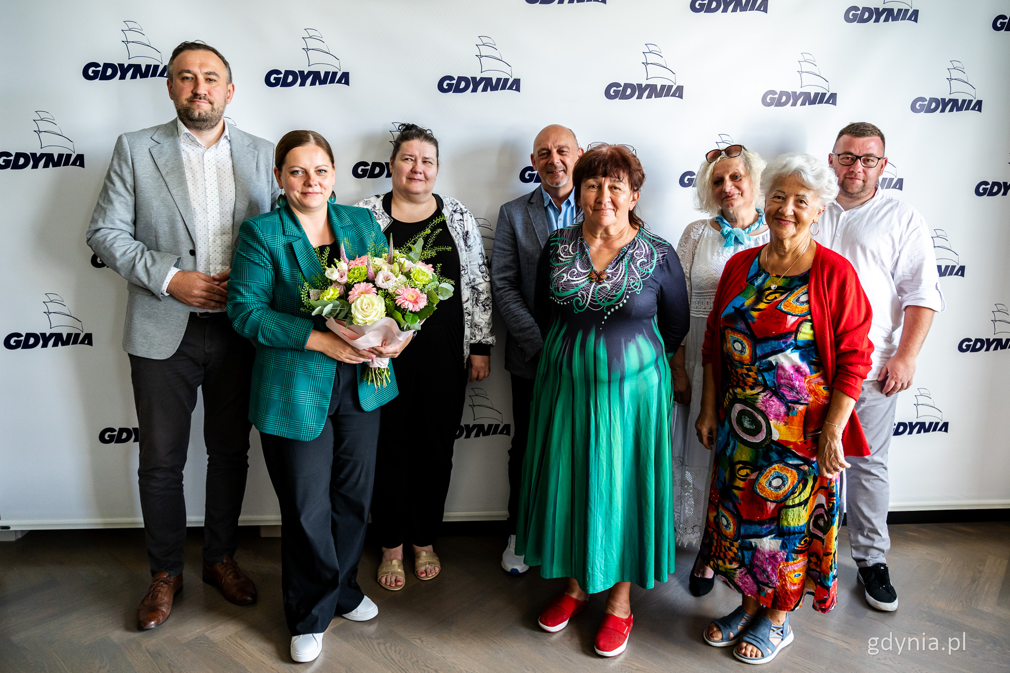 Sala w Urzędzie Miasta Gdyni, biała ściana z logotypami miasta, grupa os&oacute;b pozuje do zdjęcia