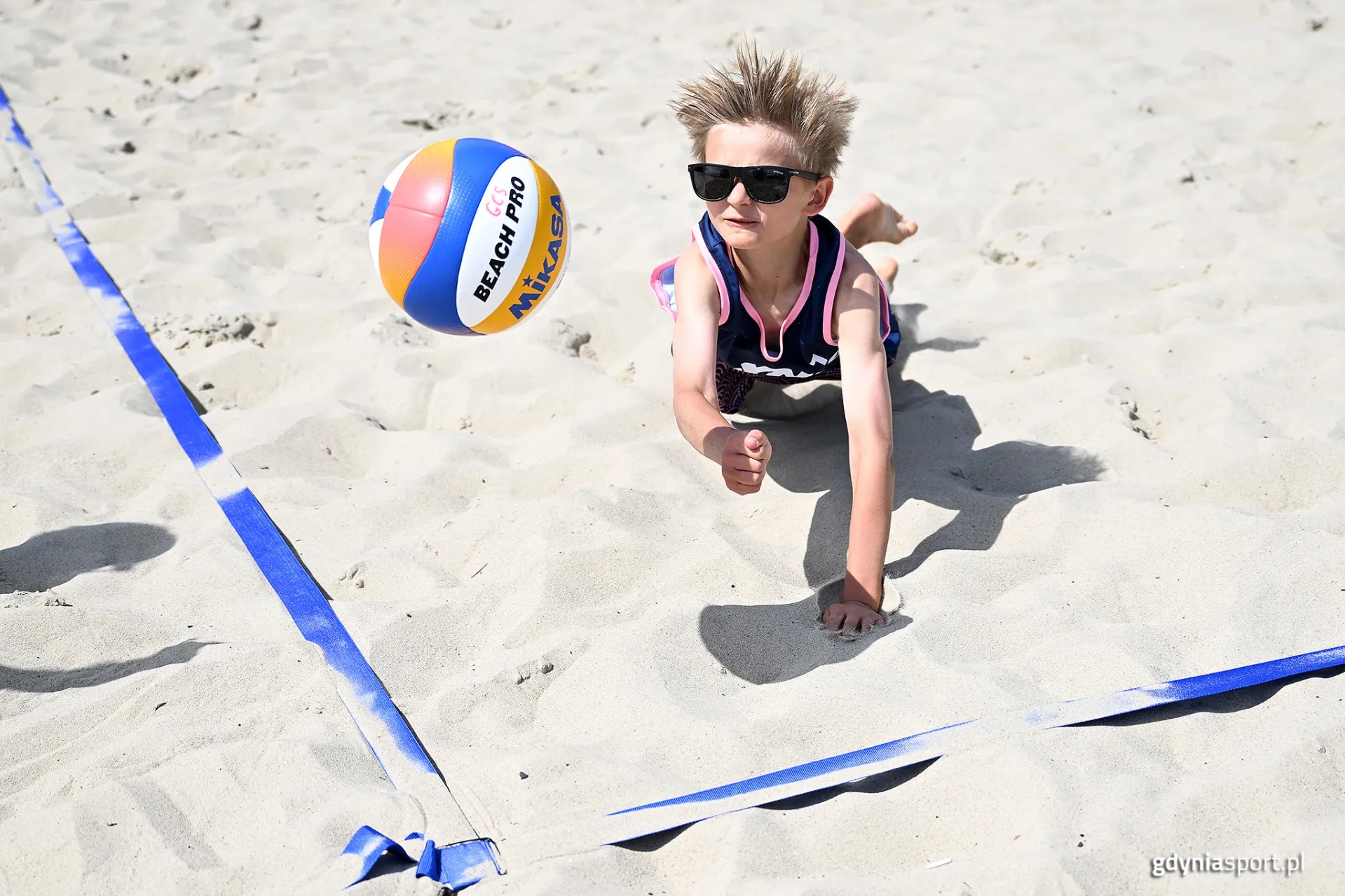 chłopiec rzucający się na piasek po piłkę