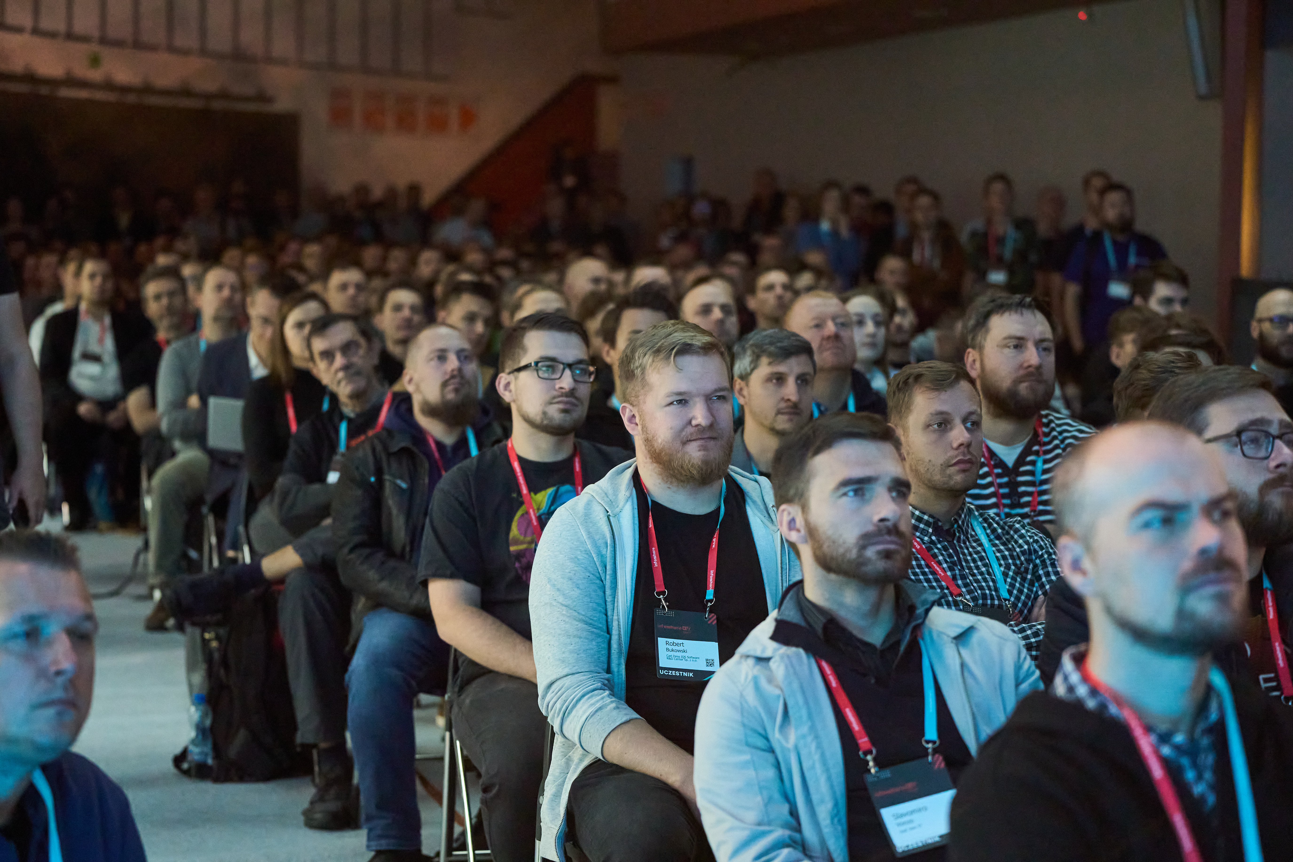 Grupa os&oacute;b siedzących na krzesłach w sali widziana od przodu