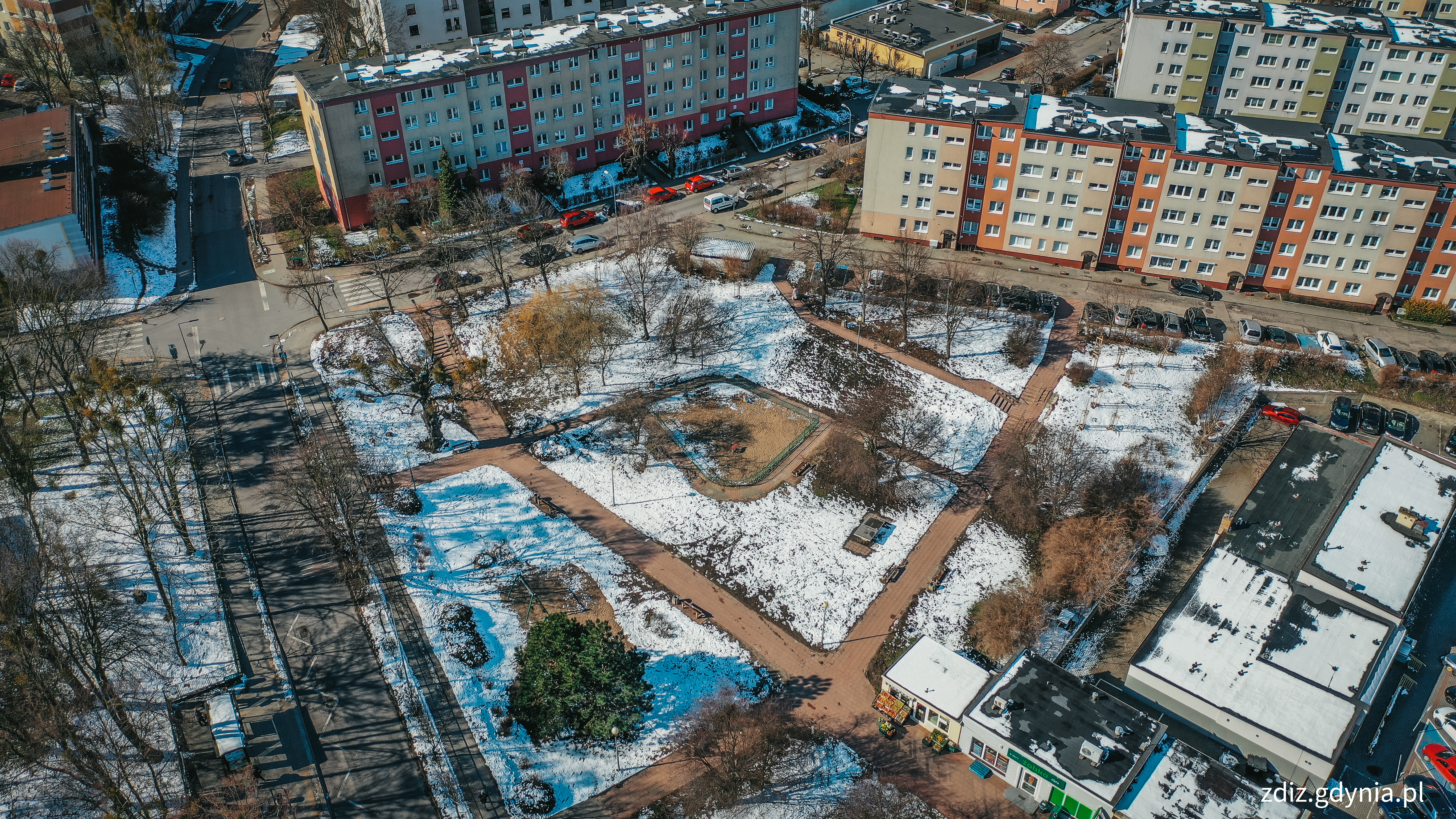 zdjęcie z góry, widoczny ośnieżony skwer na którym znajduje się plac zabaw. sprzęty zabawowe, ławki, zieleń. 