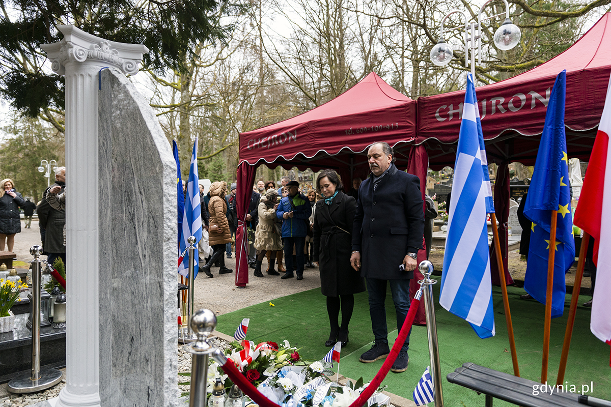 Kobieta i mężczyzna składają wieniec pod pomnikiem na cmentarzu.