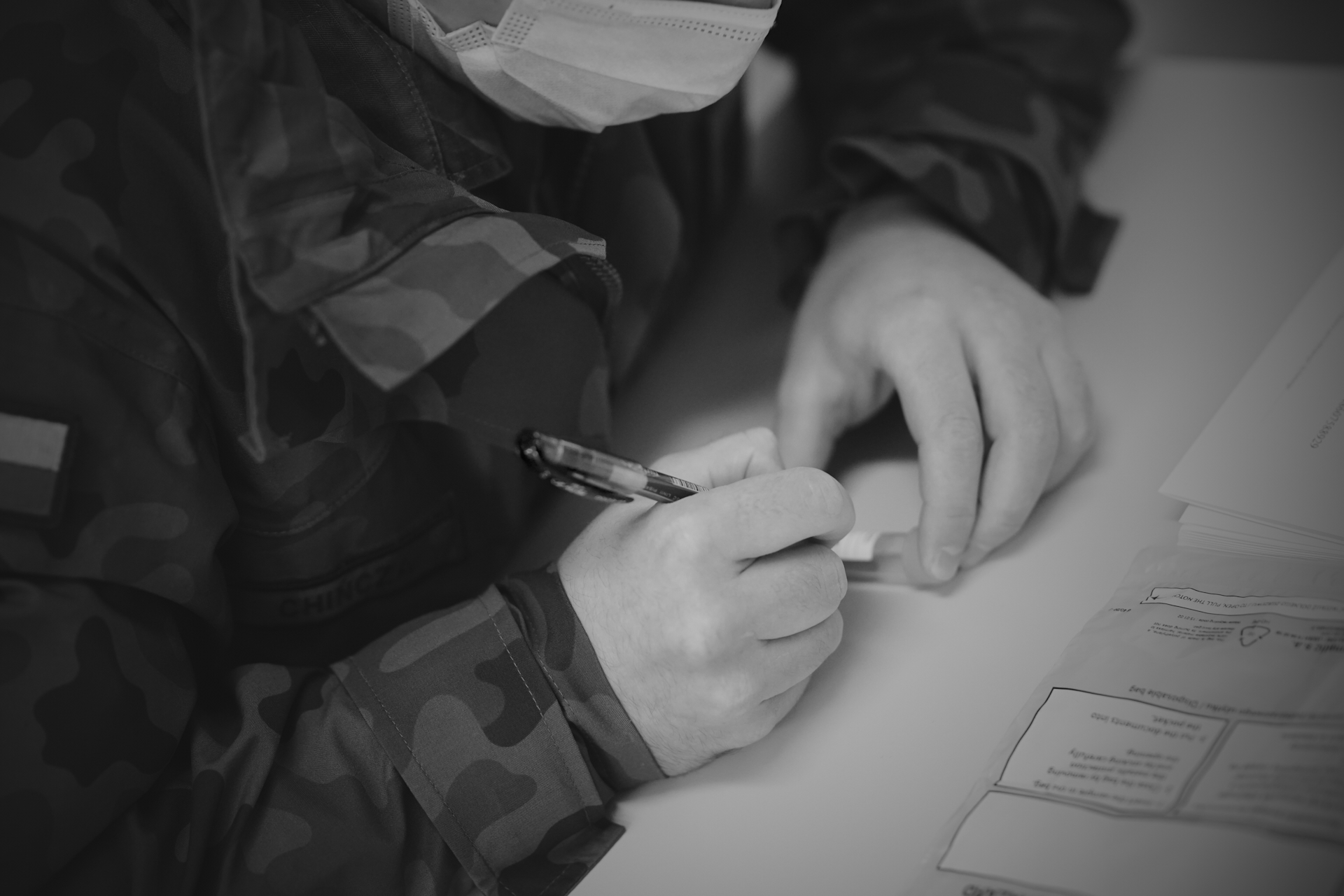 Jeden z żołnierzy w maseczce i z długopisem w ręku podpisuje próbkę. Przed nim na stole leży przezroczysty woreczek ochronny // fot. st. chor. szt. mar. Piotr Leoniak