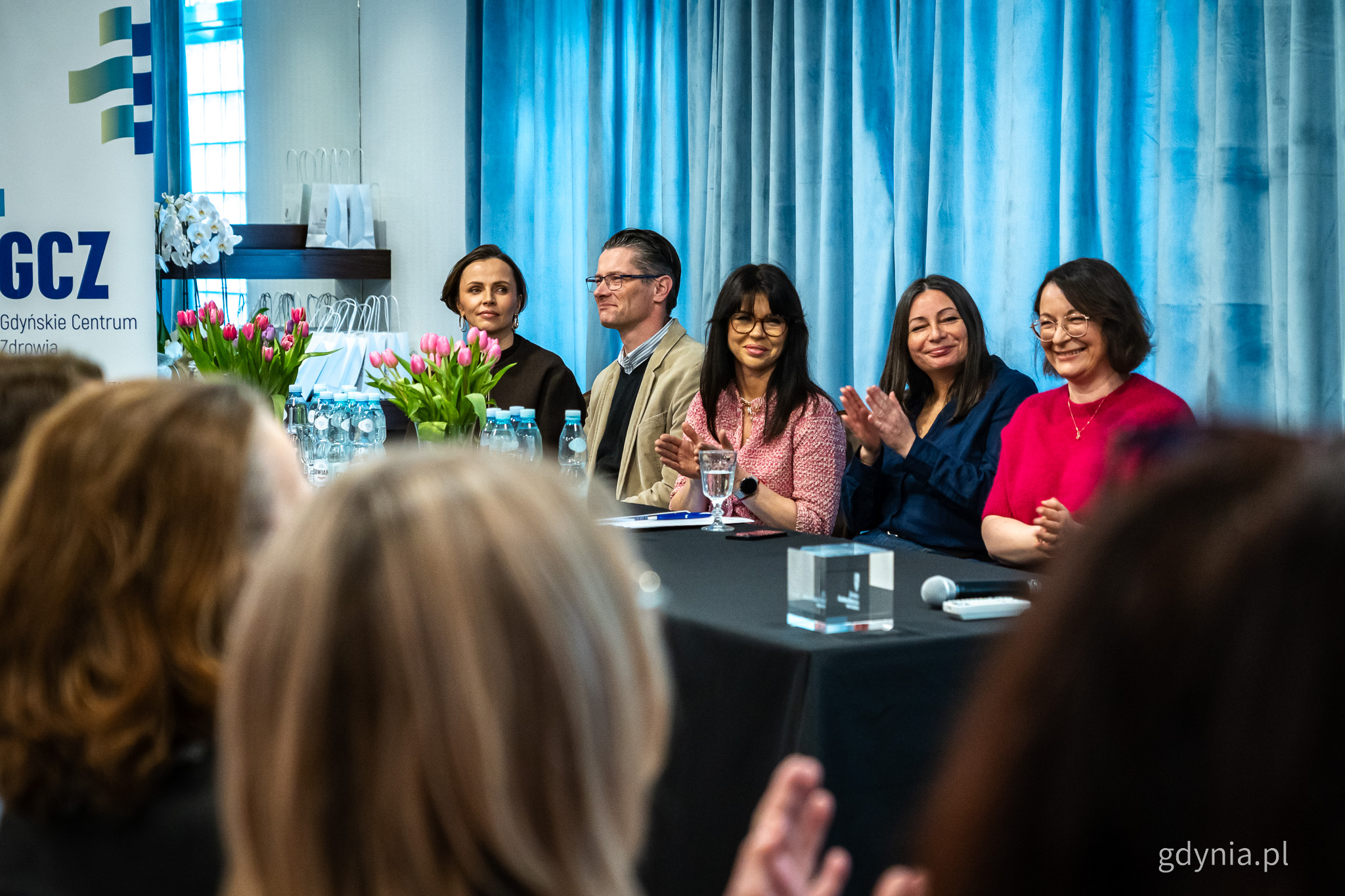 Sala konferencyjna, kilka os&oacute;b przy stole dla prelegent&oacute;w bije brawo, widoczna publiczność