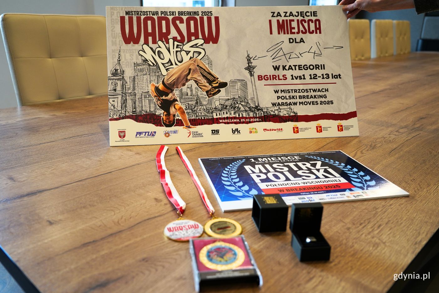 St&oacute;ł na kt&oacute;rym leżą trzy medale, sygnet oraz dwie tabliczki, na kt&oacute;rych znajduje się opis osiągnieć Laury Chałubowicz.