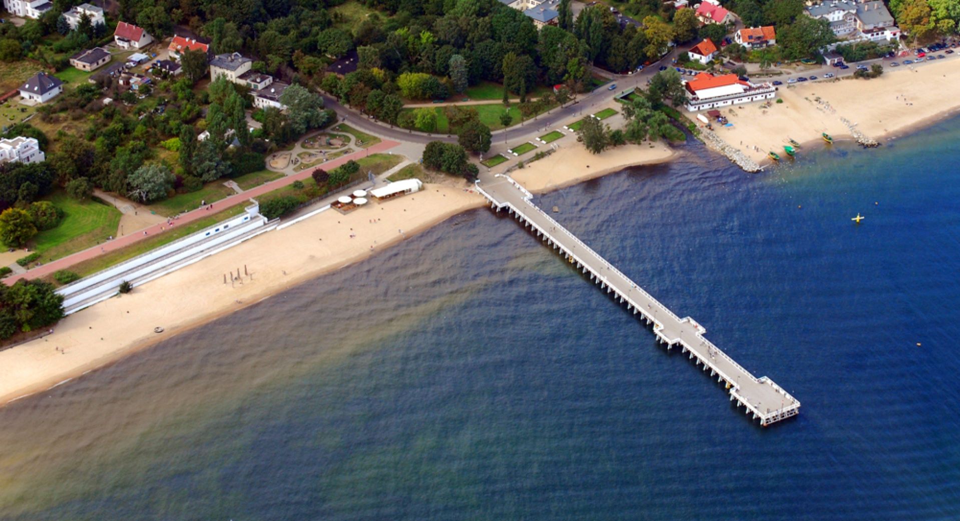 Zdjęcie lotnicze fragmentu Orłowa, molo, plaża, zabudowania i zieleń, fragment morza, dzień