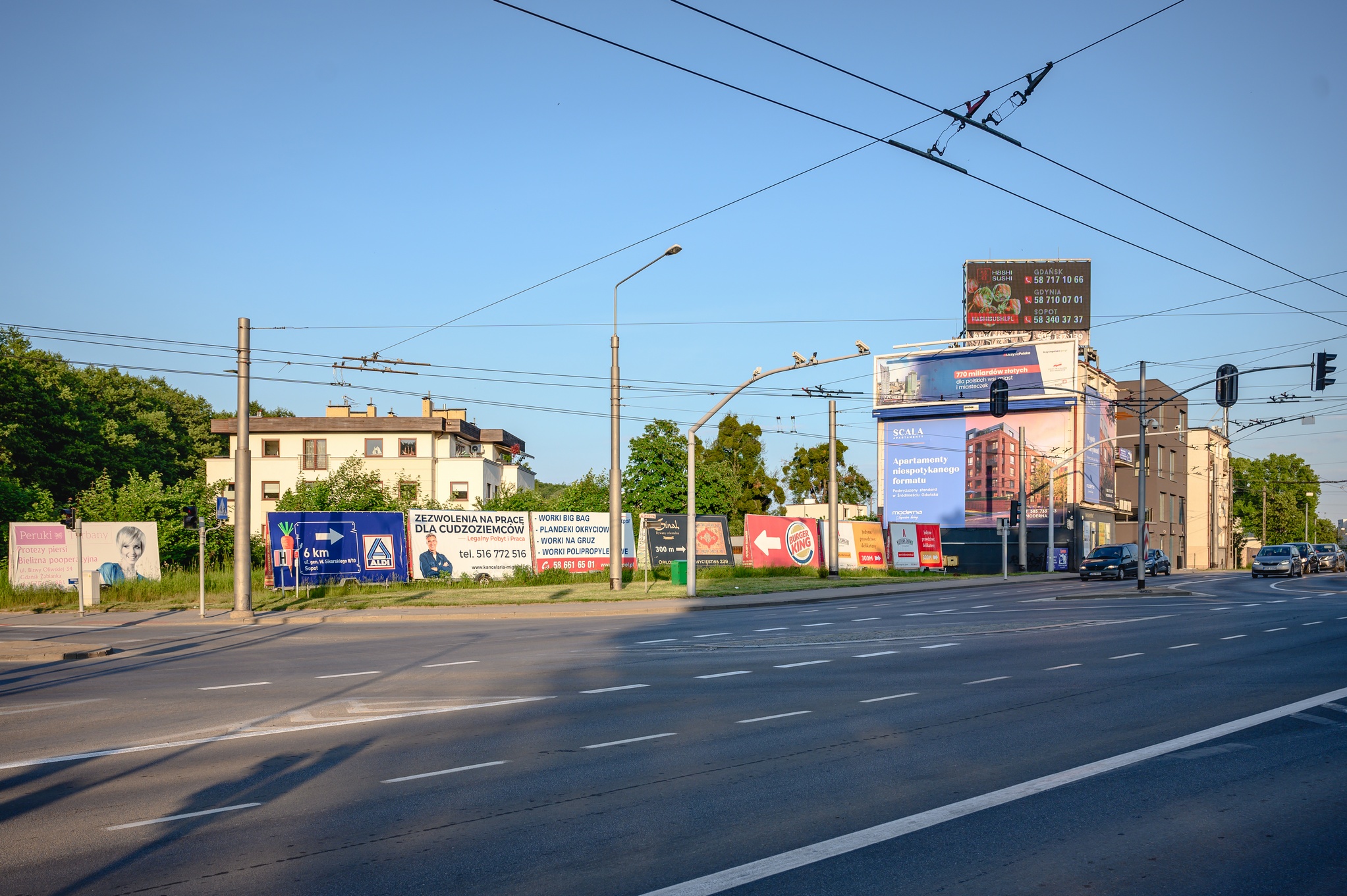 Aleja Zwycięstwa w Gdyni na fotografii ruch uliczny oraz po lewej stronie budynek z reklamami oraz reklamy rozstawione wzdłuż drogi, fot. t.Kamiński