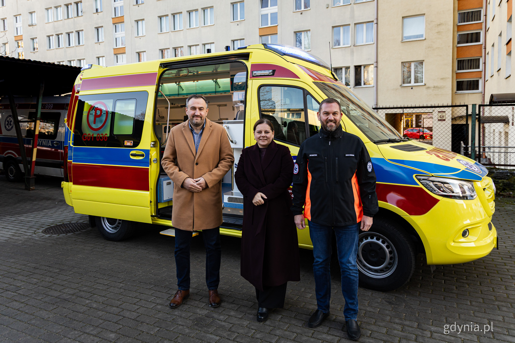 Ż&oacute;łta karetka na placu przy Miejskiej Stacji Pogotowia Ratunkowego, do zdjęcia pozują Tomasz Augustyniak, Aleksandra Kosiorek i Jacek Adamonis