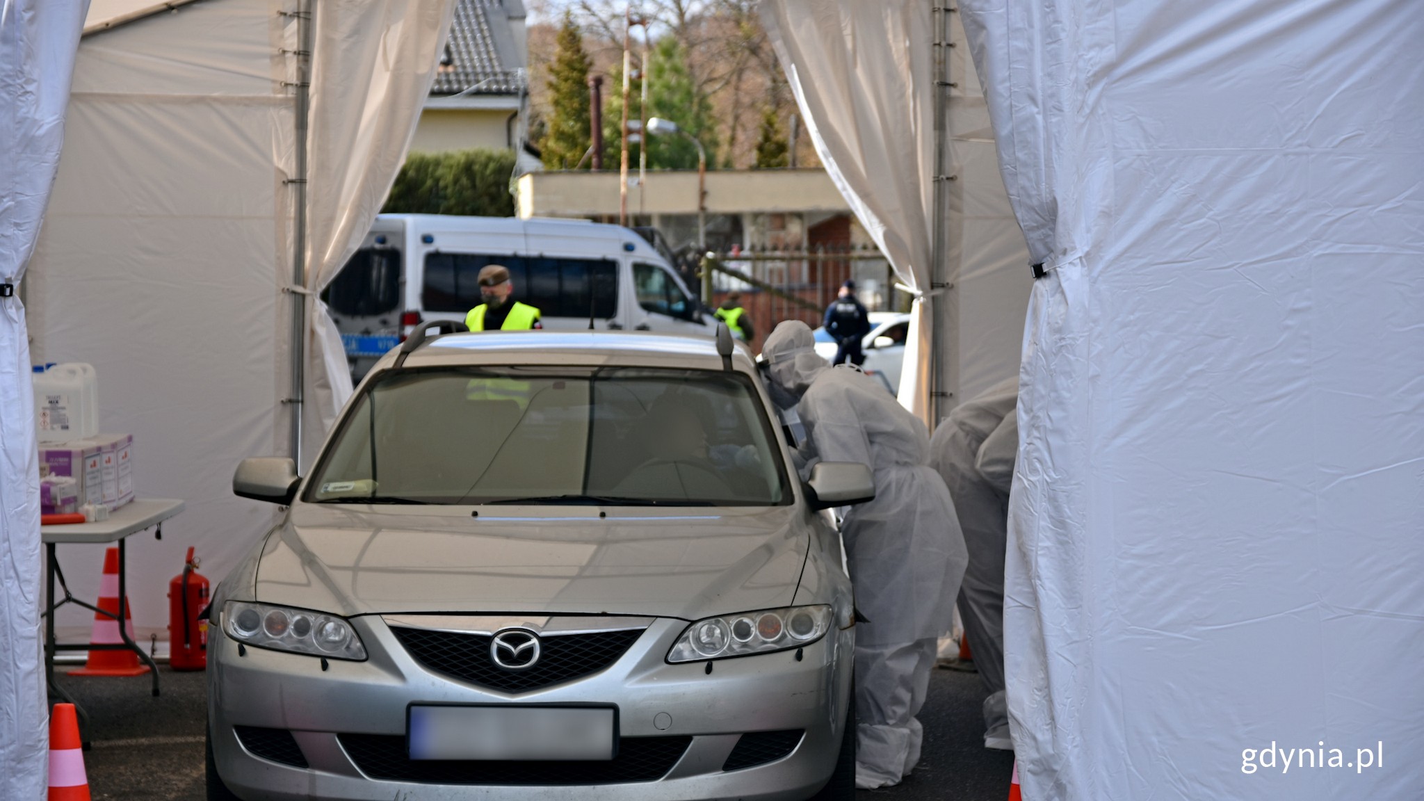 Centrum testowe Covid-19 drive-thru przy Instytucie Medycyny Morskiej i Tropikalnej w Gdyni. W białym namiocie stoi srebrne auto. wolontariusze pobierają wymaz od kierowcy // fot. Magdalena Czernek