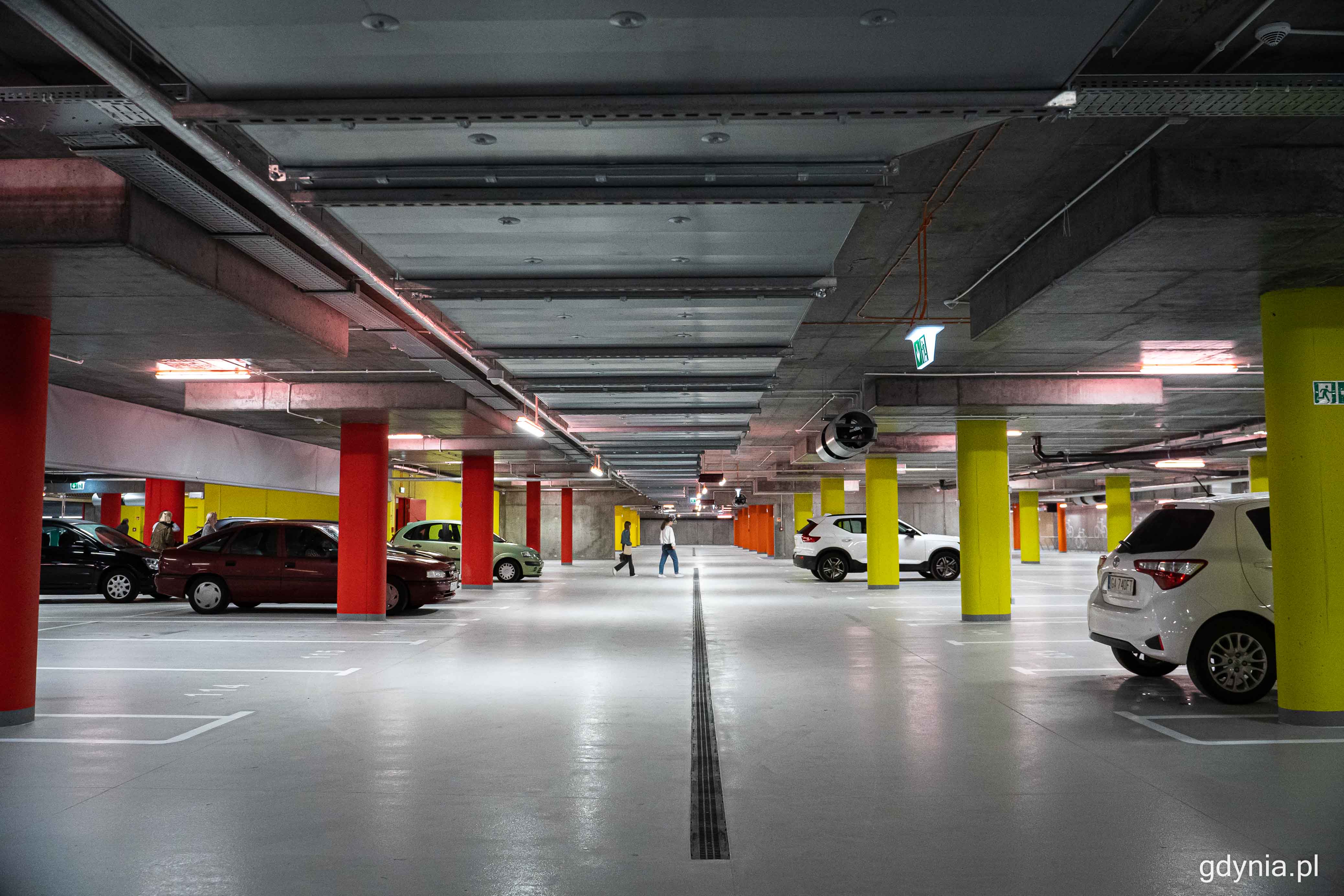 Parking podziemny w Gdyni, kolorowe filary, puste miejsca, kilka samochodów, dwie osoby w środku kadru