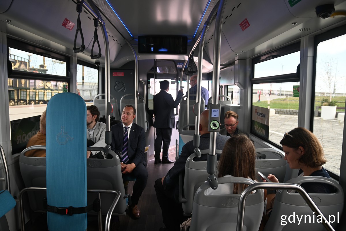 Wnętrze autobusu wodorowego, kilka osób siedzi na fotelach pasażerów, autobus w ruchu