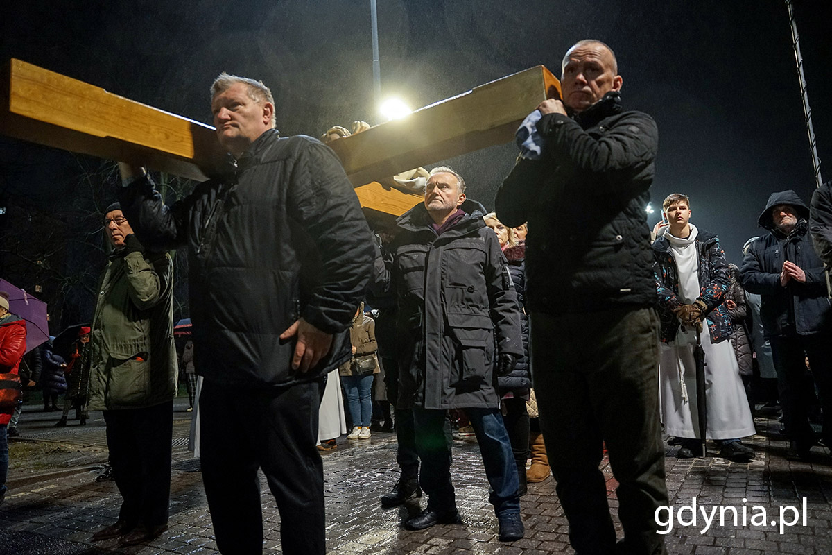 Ludzie niosą krzyż ulicami miasta podczas drogi krzyżowej.