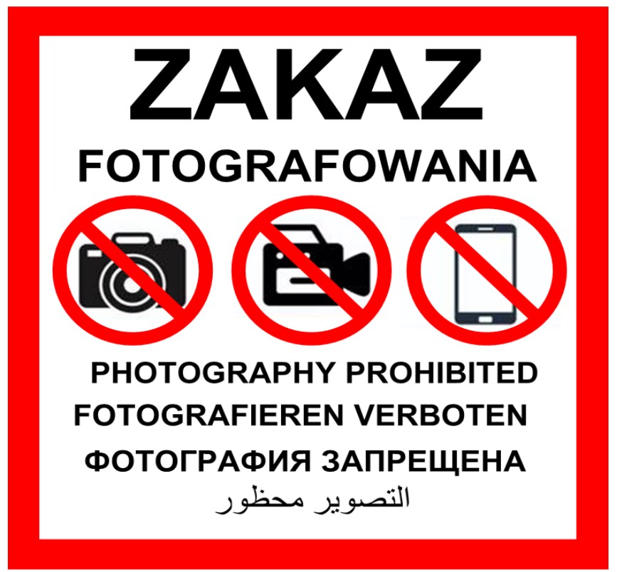 Biały znak z czerwoną obwódką, zakaz fotografowania, przekreślone ikony aparatu, kamery i smartfona oraz napisy w pięciu językach