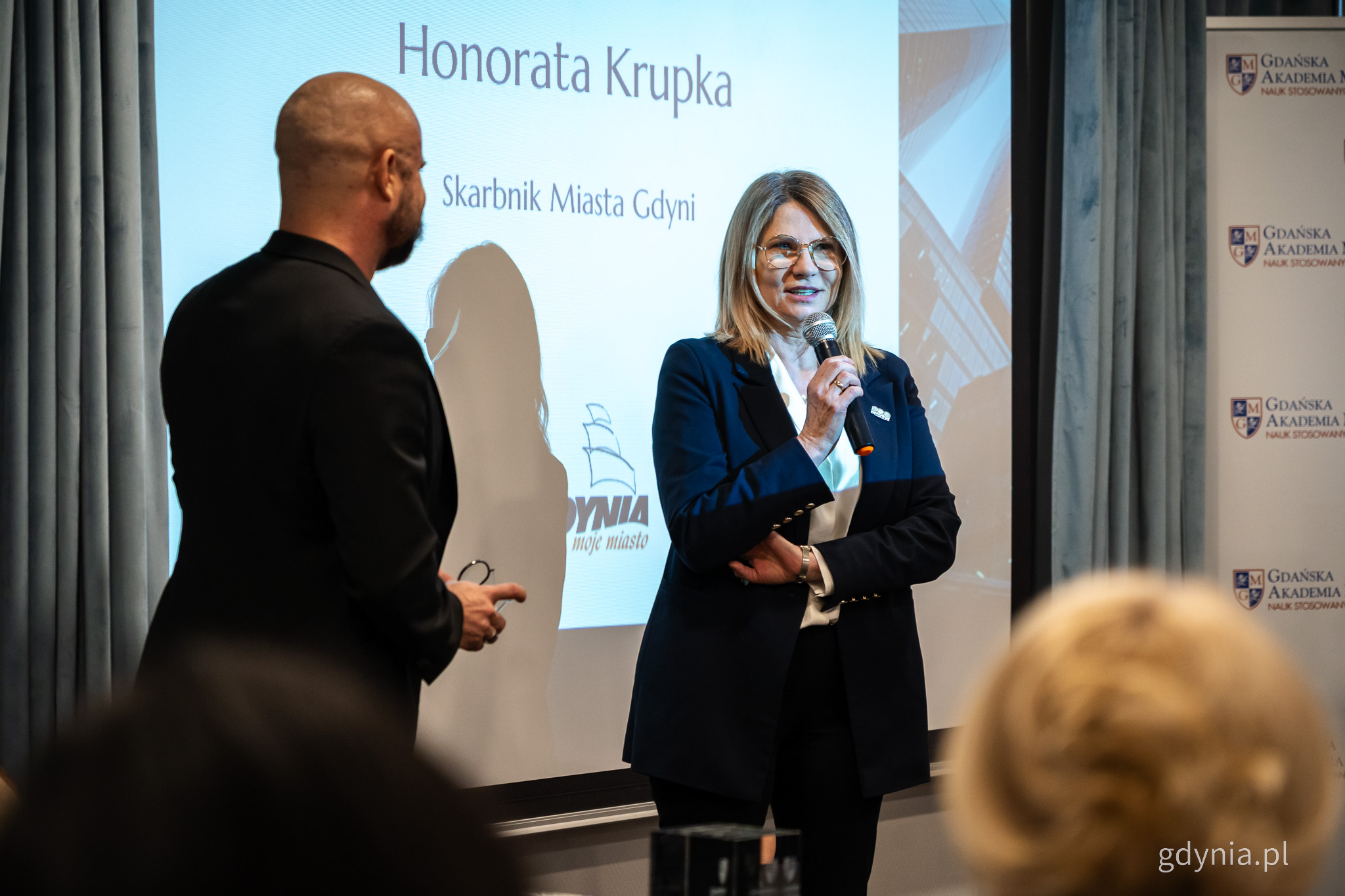 Sala konferencyjna, na ekranie slajd, na środku przemawia przez mikrofon Honorata Krupka, obok prowadzący