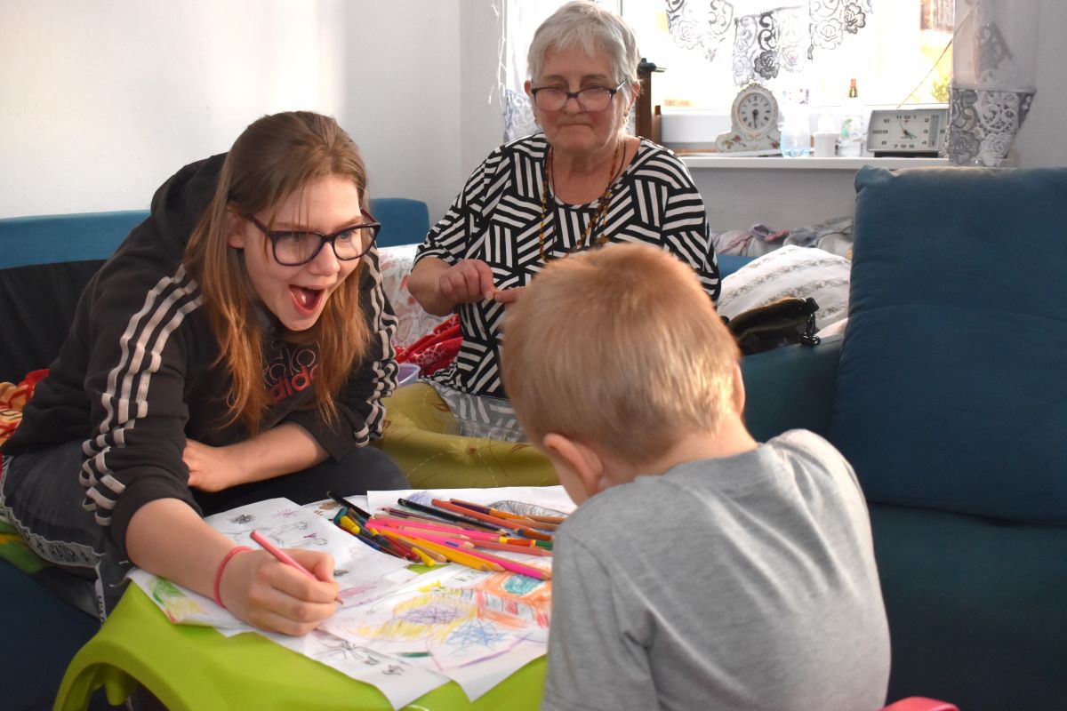 Zdjęcie prezentuje panią Teresę - rodzica zastępczego, rysującego z dwójką dzieci będących pod jej opieką. 19 letnią Agatą i 3 letnim Krzysiem. 