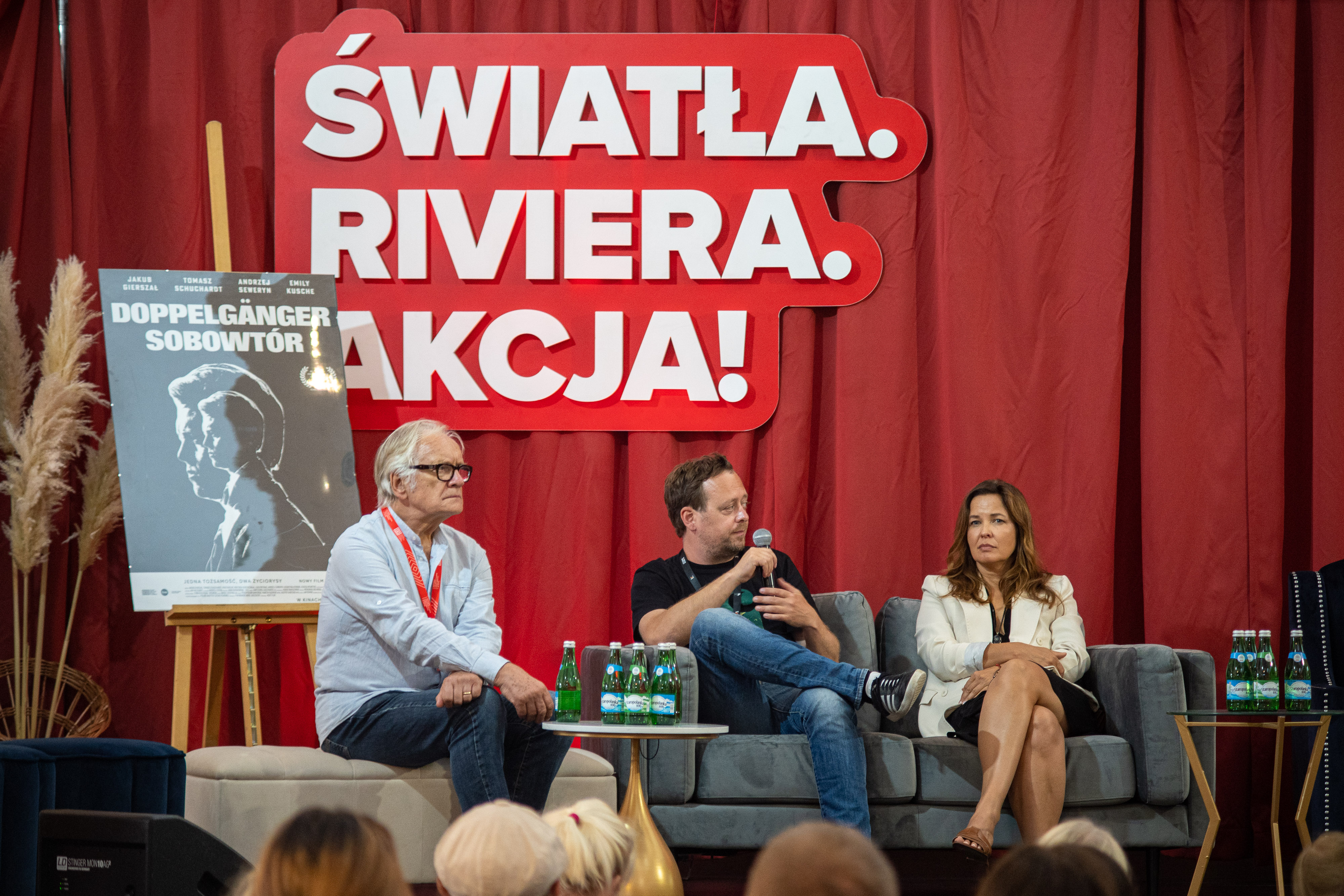 Scena w Rivierze, czerwone tło, Andrzej Seweryn siedzi na krześle, obok plakat filmu