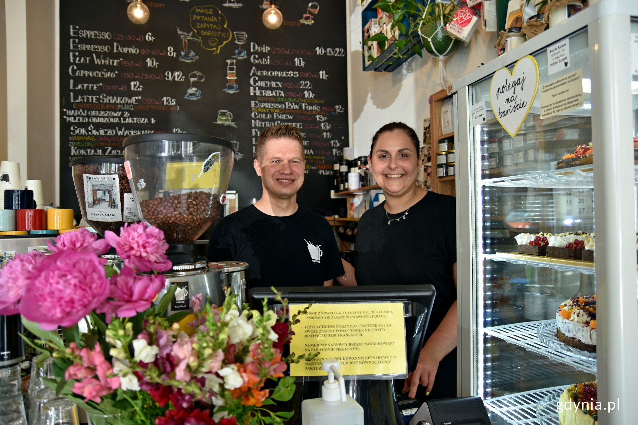 Barbara Szparagowska i Leszek Jędrasik, właściciele kawiarni „Black & White Coffee”. Za nimi tablica z menu. Na pierwszym planie lada, na której stoi ekspres, kasa i kwiaty // fot. Magdalena Czernek