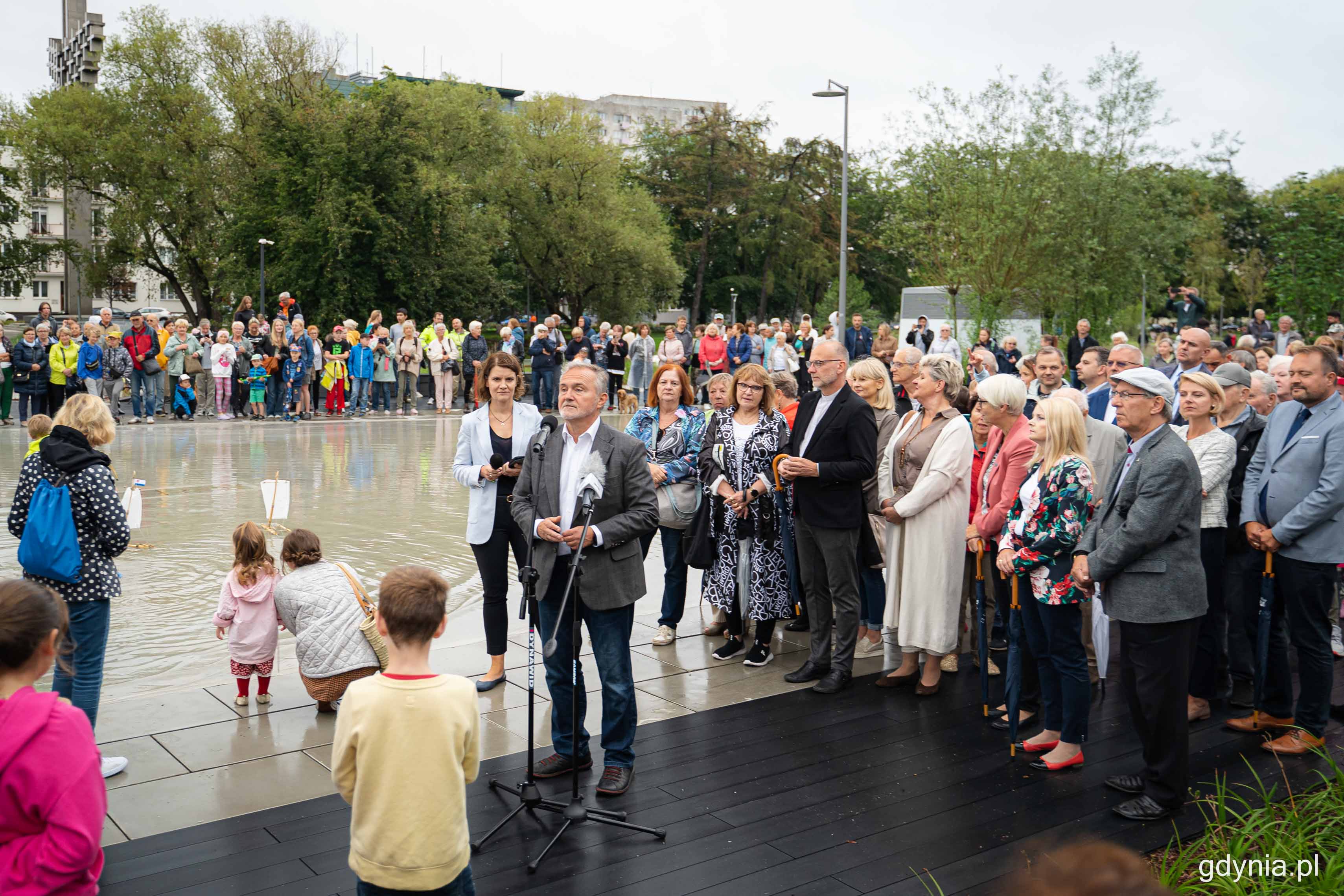 Park Centralny, sadzawka z wodą, tłum ludzi, do mikrofonu przemawia Wojciech Szczurek