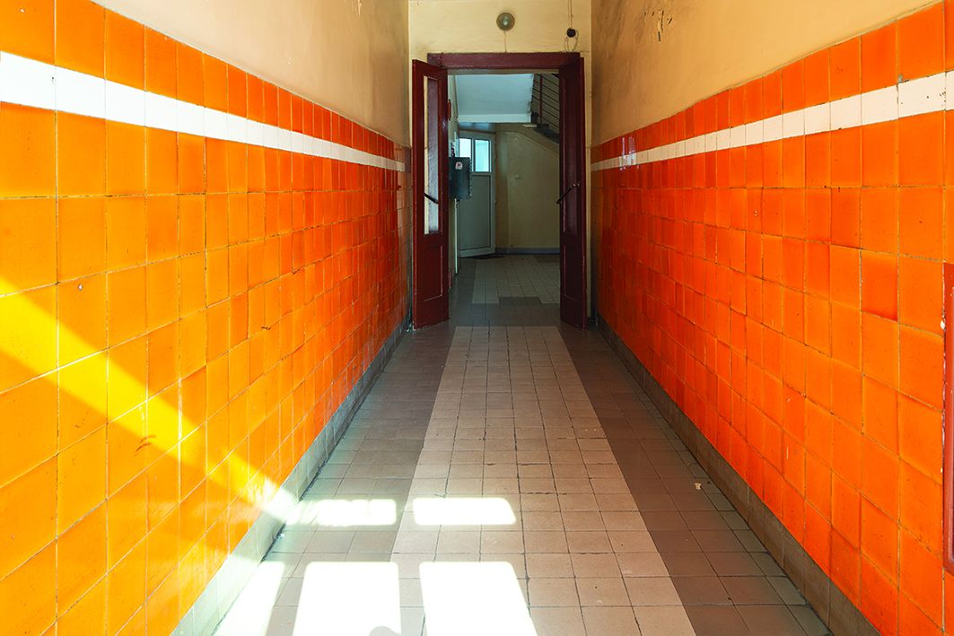 Strefa wejściowa w kamienicy przy skwerze Kościuszki 14, dolne partie ścian wykończone ceramicznymi pomarańczowymi płytkami z wykończeniem z białym paskiem.