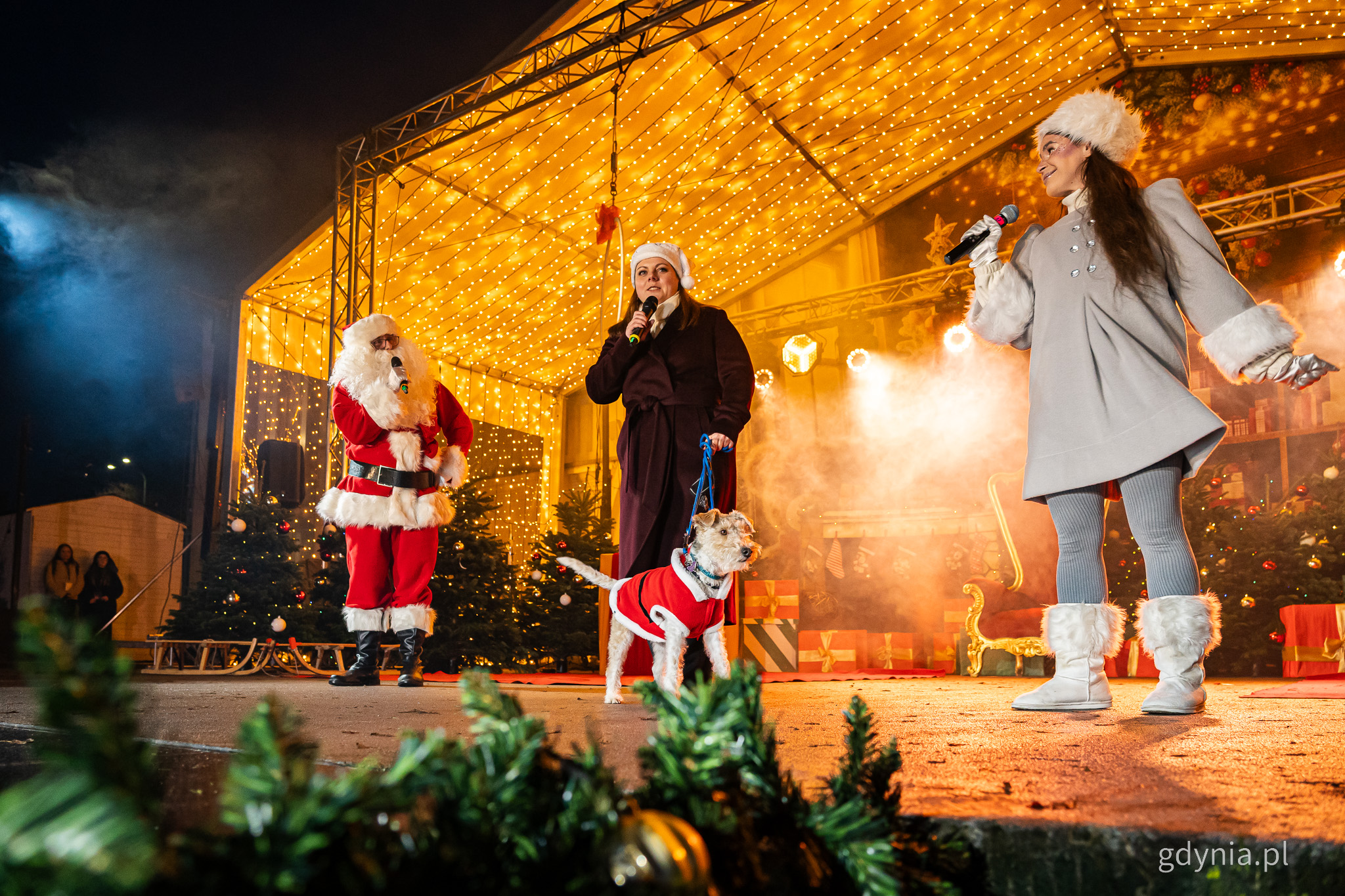 Prezydent Gdyni Aleksandra Kosiorek, mikołaj i aktorka na scenie w muszli koncertowej, dekoracje świąteczne, prezydent Gdyni trzyma na smyczy psa