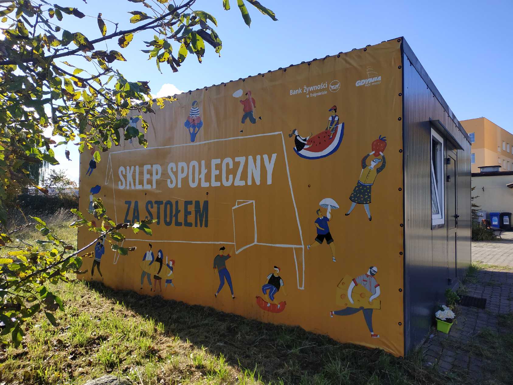 Pomarańczowy kontener z napisem: sklepik społeczny