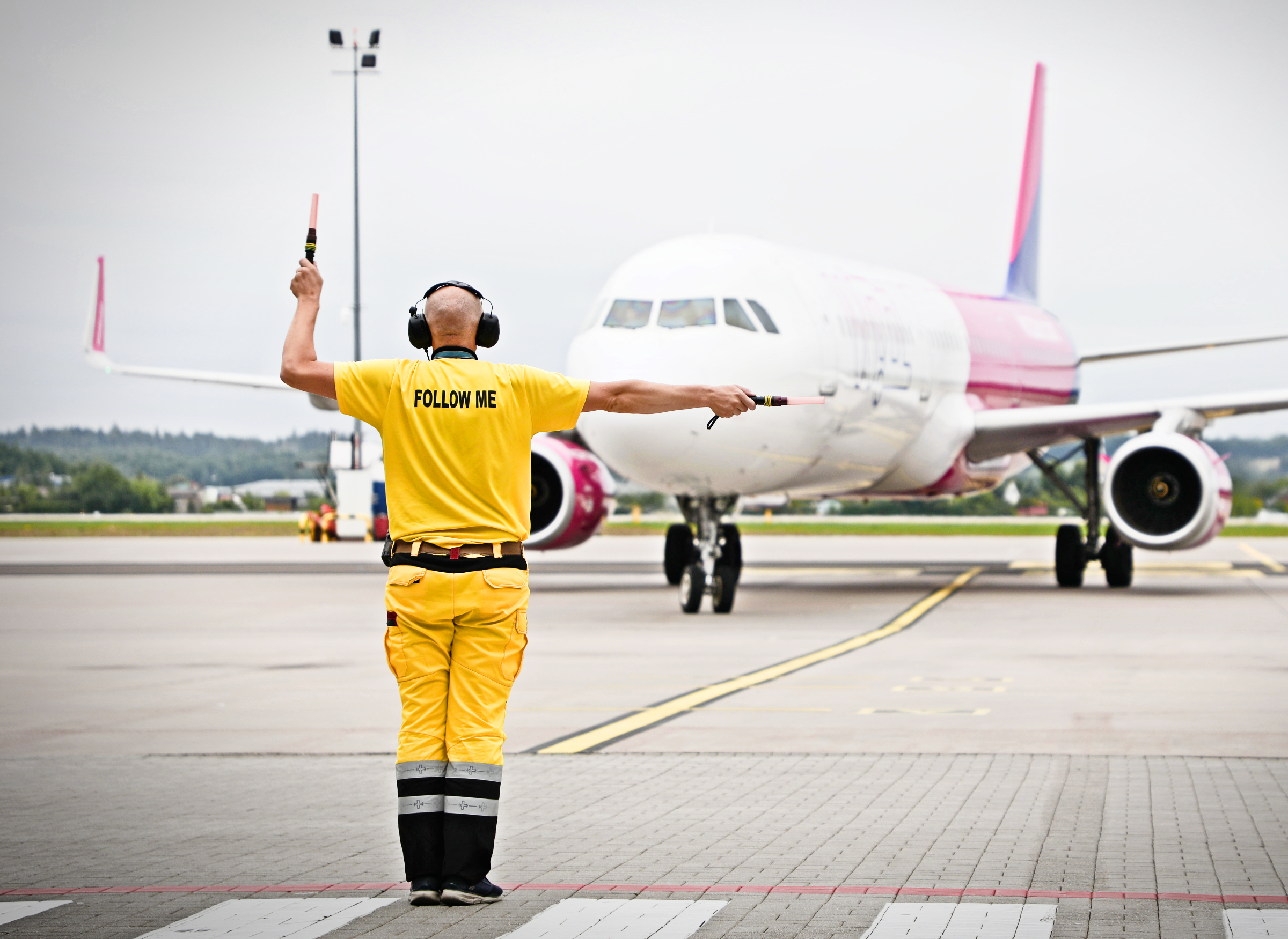 Pracownik na płycie lotniska zwrócony twarzą w stronę samolotu Wizz Air