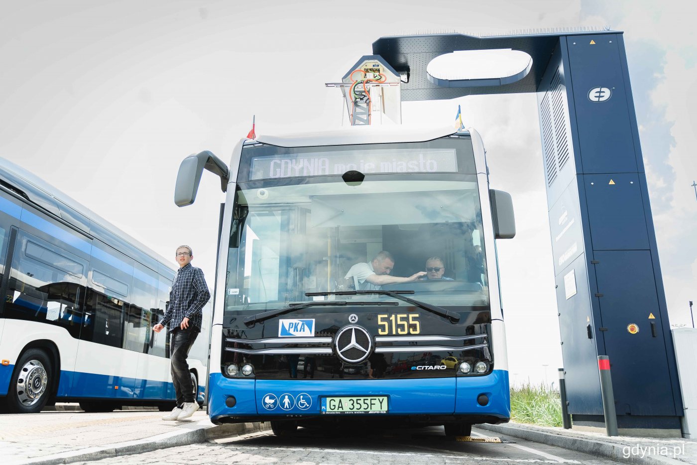 Autobus na stacji ładowania, w tle niebo, z pojazdu wychodzi młody mężczyzna