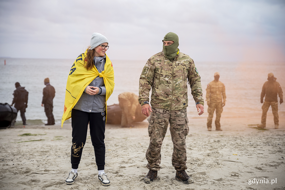 Kobieta i komandos stoją na plaży.