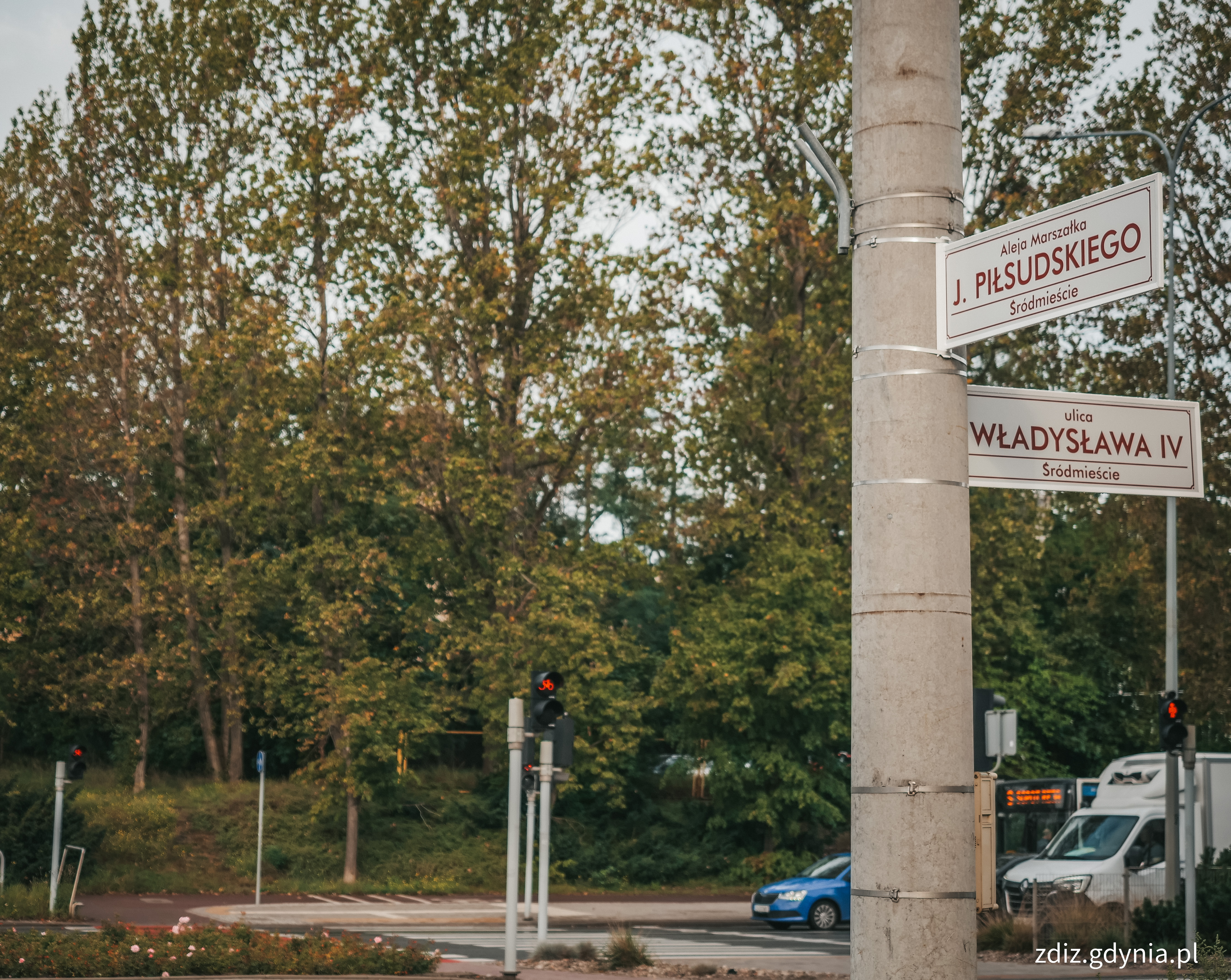 tabliczki z nazwami ulic na słupie, w tle zieleń i droga