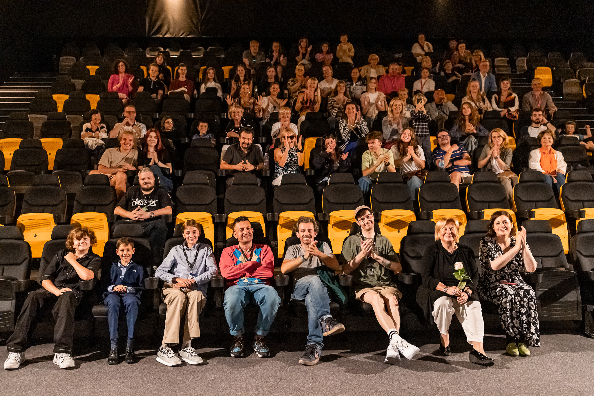 Sala kinowa, widzowie w fotelach, w pierwszym rzędzie pozują twórcy filmu