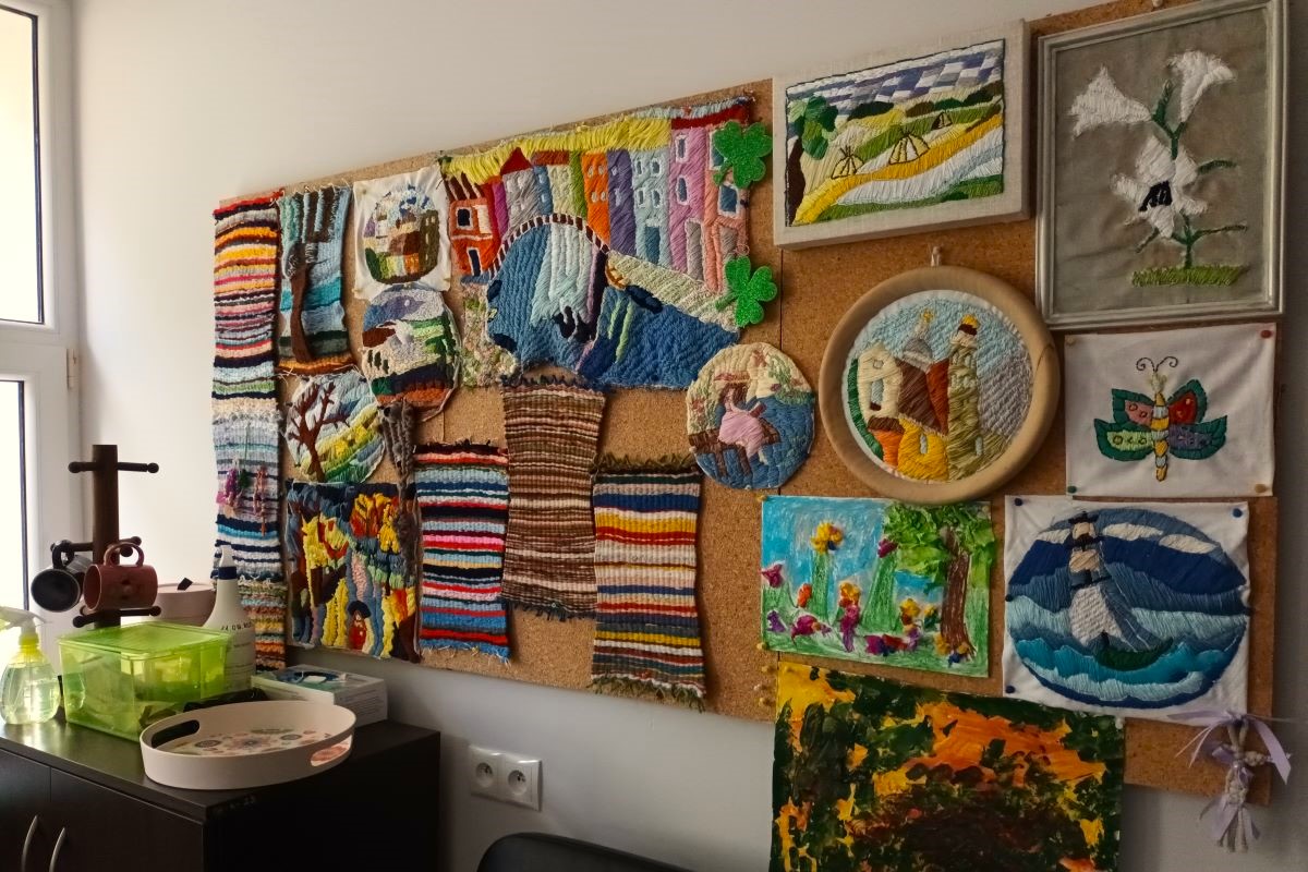 Na zdjęciu widać obrazy wytworzone techniką wyszywania. Wśród nich motyl, łódka na morzu, uliczka miejska, pole po okresie żniw.