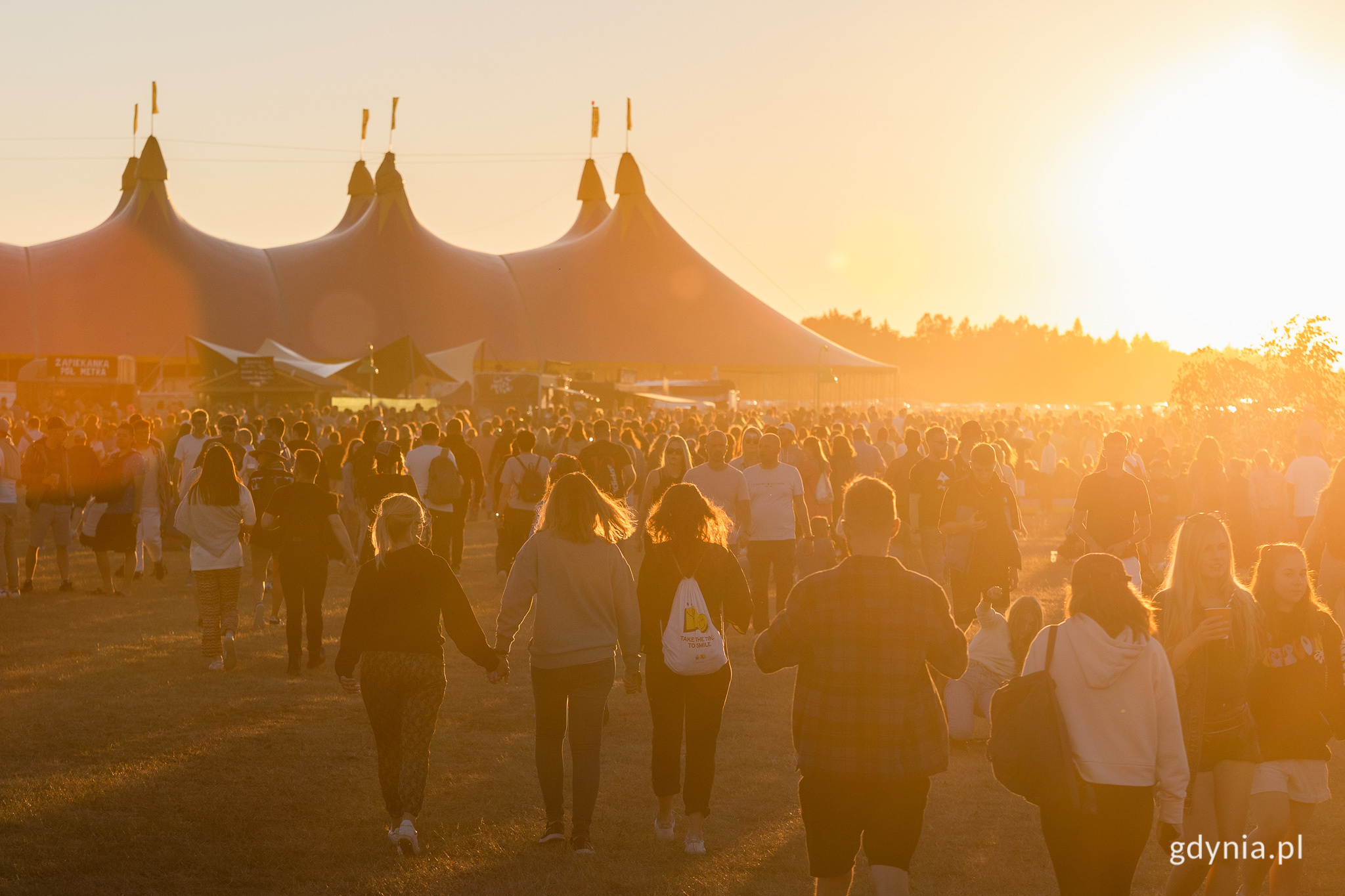 Tłum ludzi na festiwalu Open'er festival e świetle zachodzącego słońca, w tle wielkie namioty. Fot. Karol Stańczak