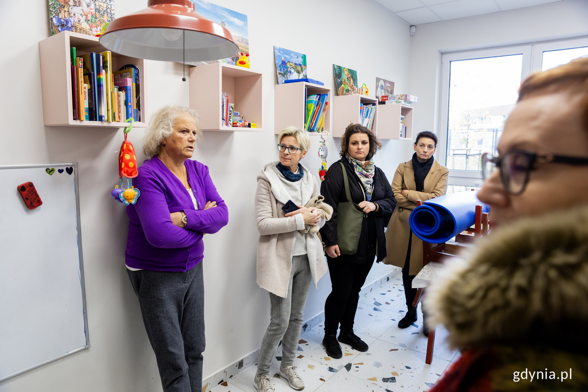 Kobieta stoi pod ściana i mówi do innych kobiet.