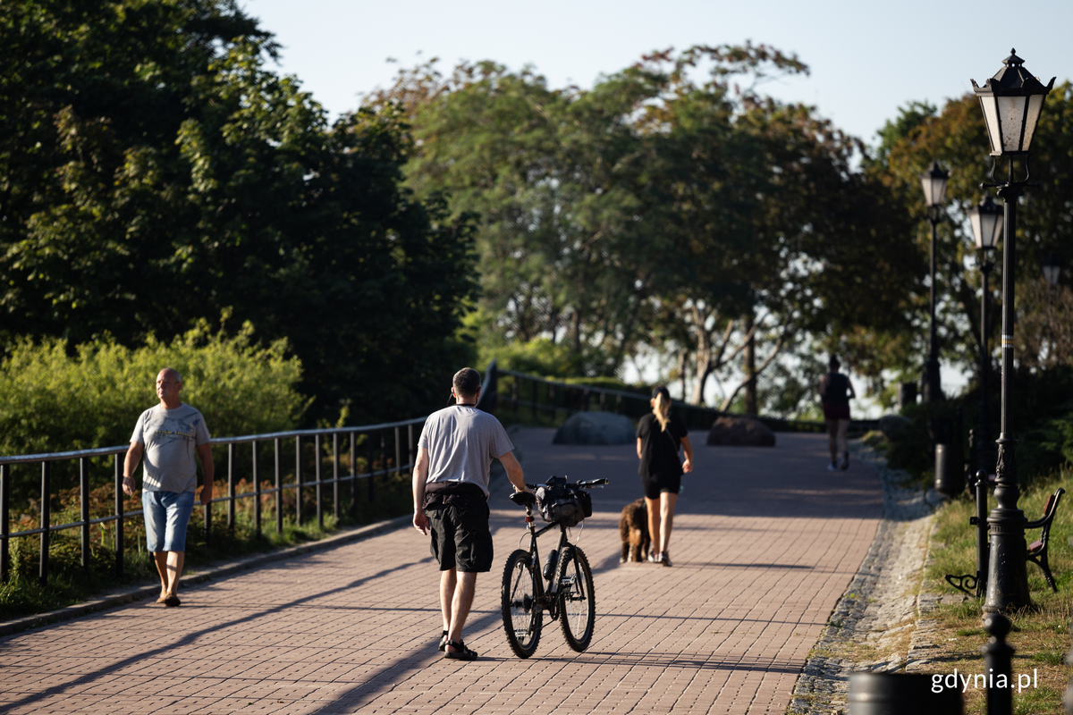 Mężczyzna prowadzi rower po promenadzie. 