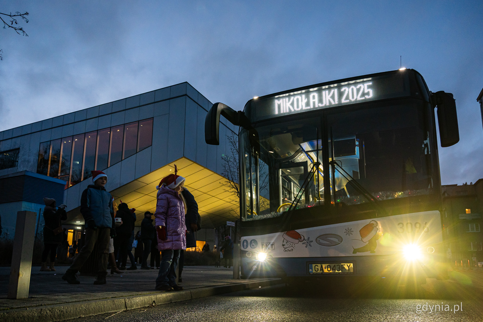 Ulica Armii Krajowej, trolejbus z napisem Mikołajki na wyświetlaczu, obok ludzie, w tle budynek Gdyńskiego Centrum Filmowego