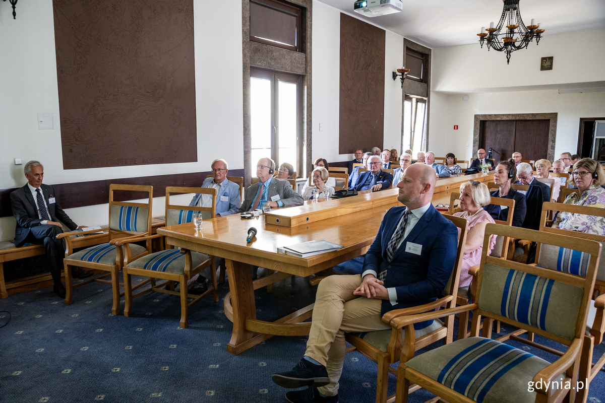 Wiceprezydent Gdyni siedzi na sali konferencyjnej z innymi uczestnikami konferencji.