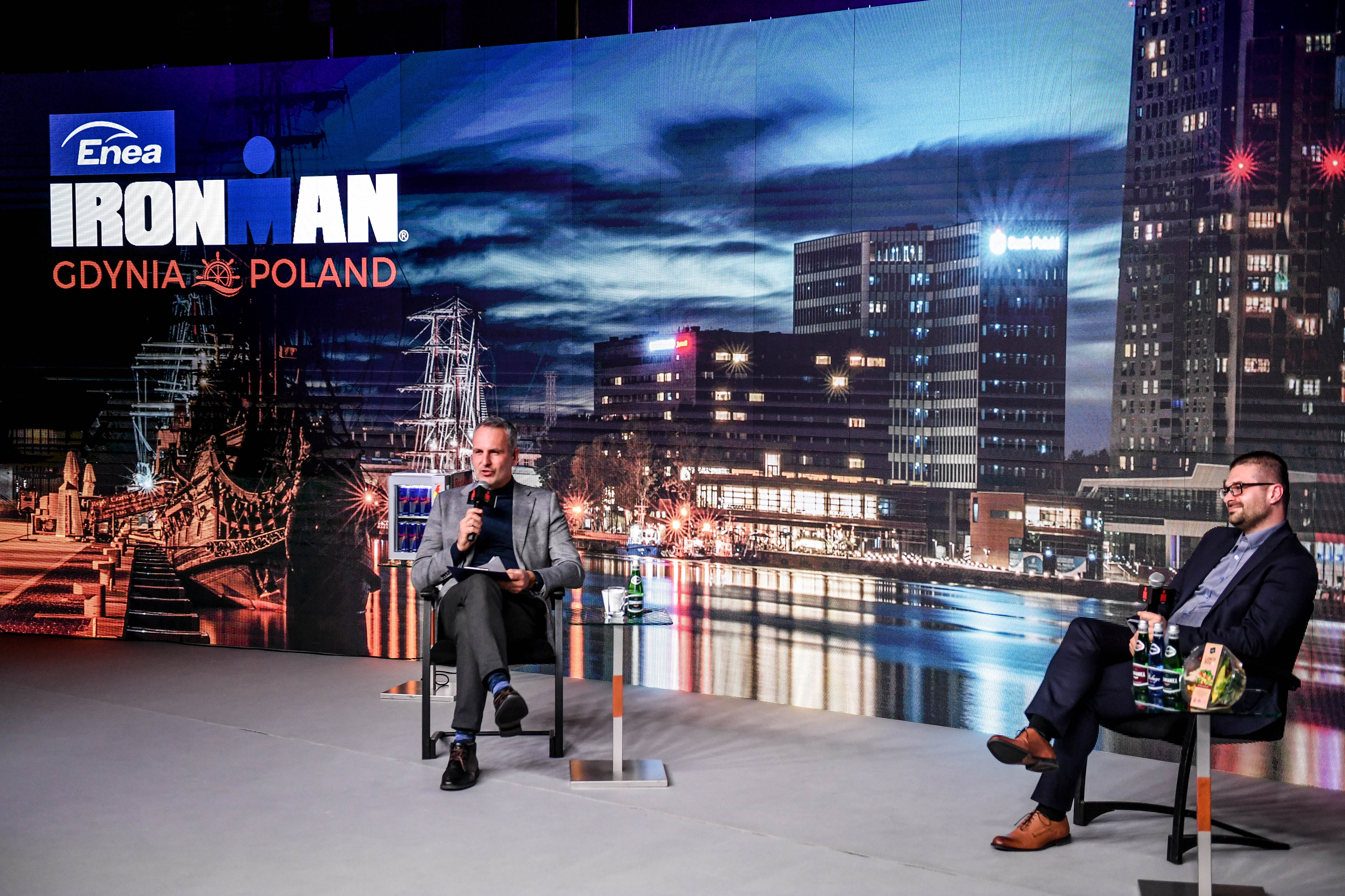 Na zdjęciu widzimy prowadzącego konferencję dziennikarza Jacka Kurowskiego oraz dyrektora zawodów Michała Drelicha. Obaj znajdują się na wielkiej scenie, siedząc na krzesłach.
