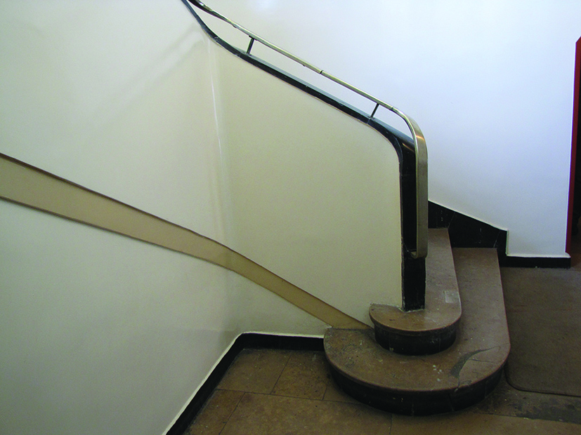 ← Początek schodów w kamienicy przy ul. Świętojańskiej 44. Zaokrąglone pierwsze stopnie całego ciągu schodów z metalową balustradą.