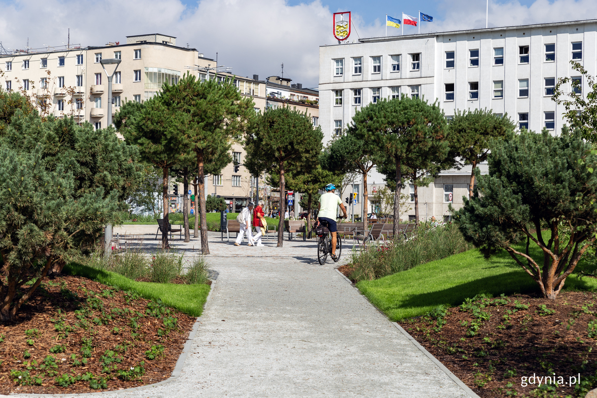 Park Centralny, ścieżka, w tle Urząd Miasta Gdyni, zieleń, drzewa, rowerzysta w środku kadru, ludzie w tle