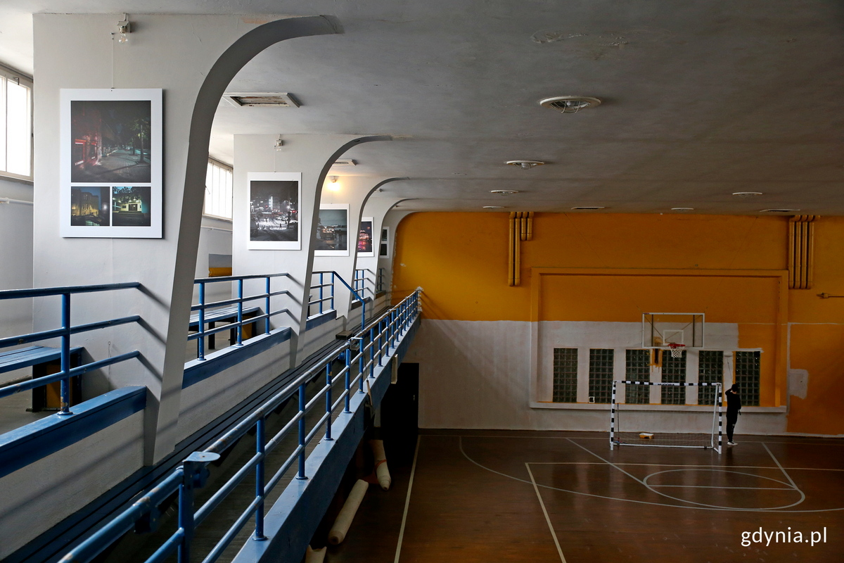 Żółte ściany hali sportowej pokrywa stopniowo jasny popiel, na filarach eksponowane są fotografie. Fot. Przemysław Kozłowski