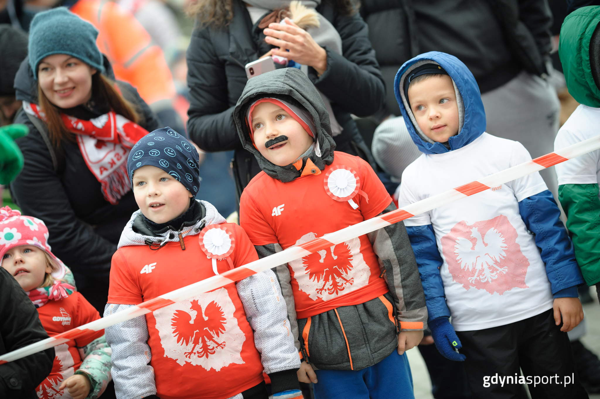 Trójka chłopców w biało-czerwonych koszulkach na starcie Biegu Niepodległości