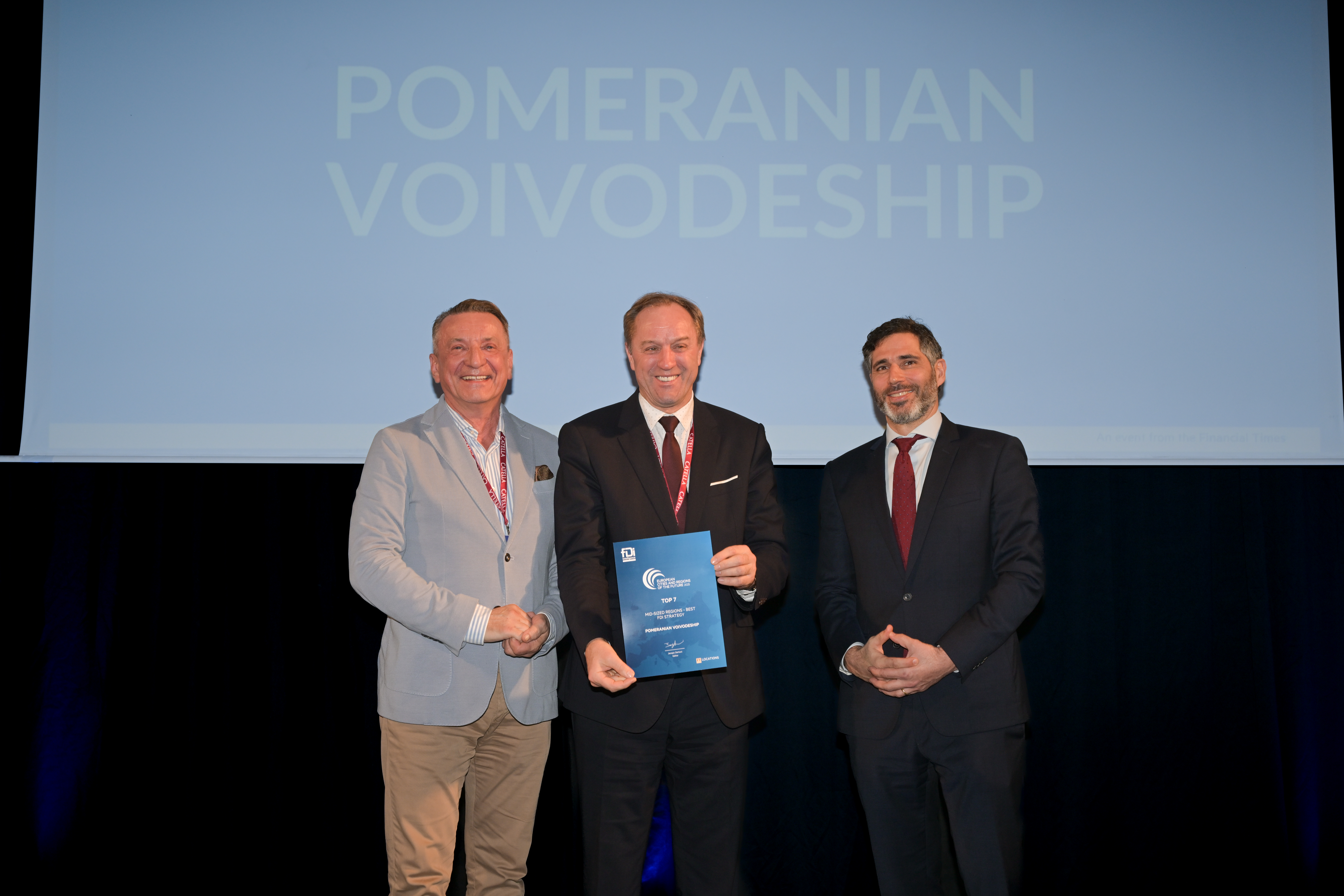 Scena, ciemne pomieszczenie, na środku wicemarszałek i marszałek województwa odbierający nagrodę, obok prowadzący wydarzenie